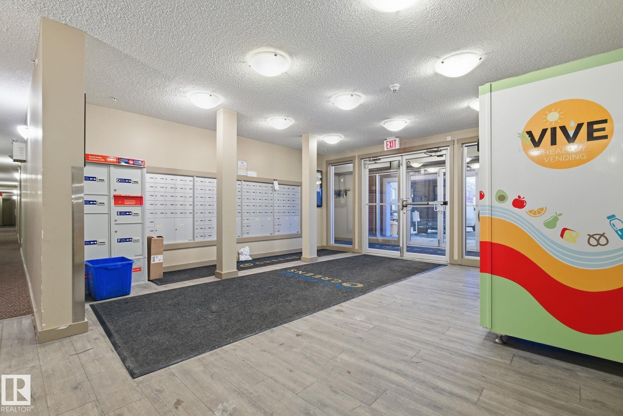 Building entry with light wood-finish flooring, multiple flush-mount ceiling lights, and two sets of glass entry doors - 424 1510 Watt Drive, Edmonton, AB