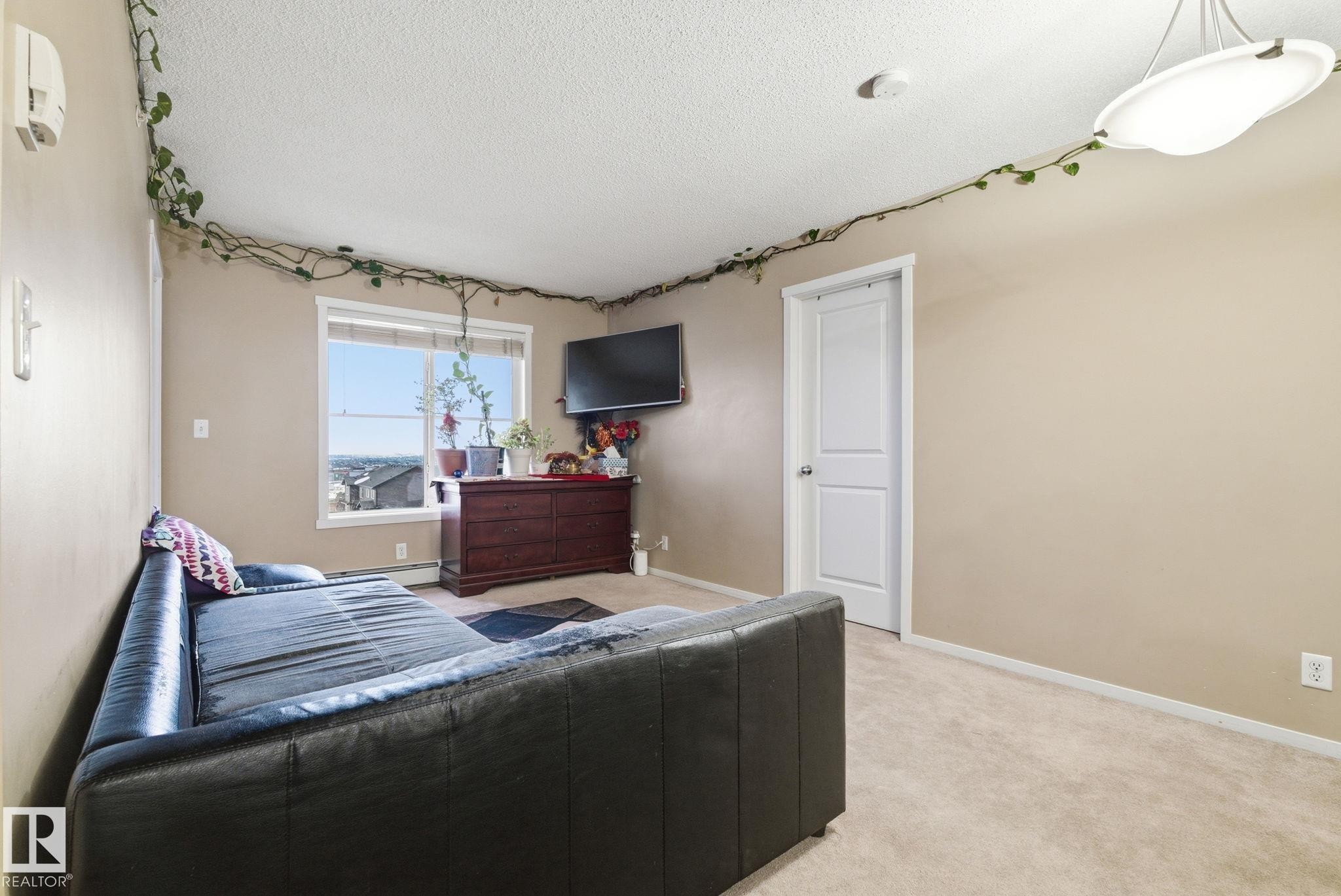 Carpeted room featuring a large window, a ceiling-mounted light fixture, and a white interior door - 424 1510 Watt Drive, Edmonton, AB