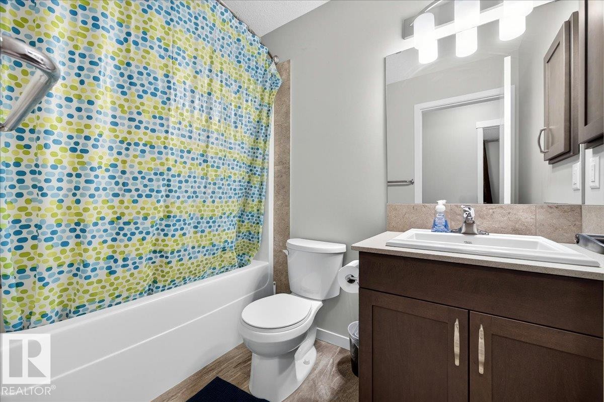 Bathroom featuring a full-size bathtub, wood-finish flooring, a contemporary vanity with an undermount sink, a large mirror, and overhead vanity lighting - 1187 Cy Becker Road, Edmonton, AB