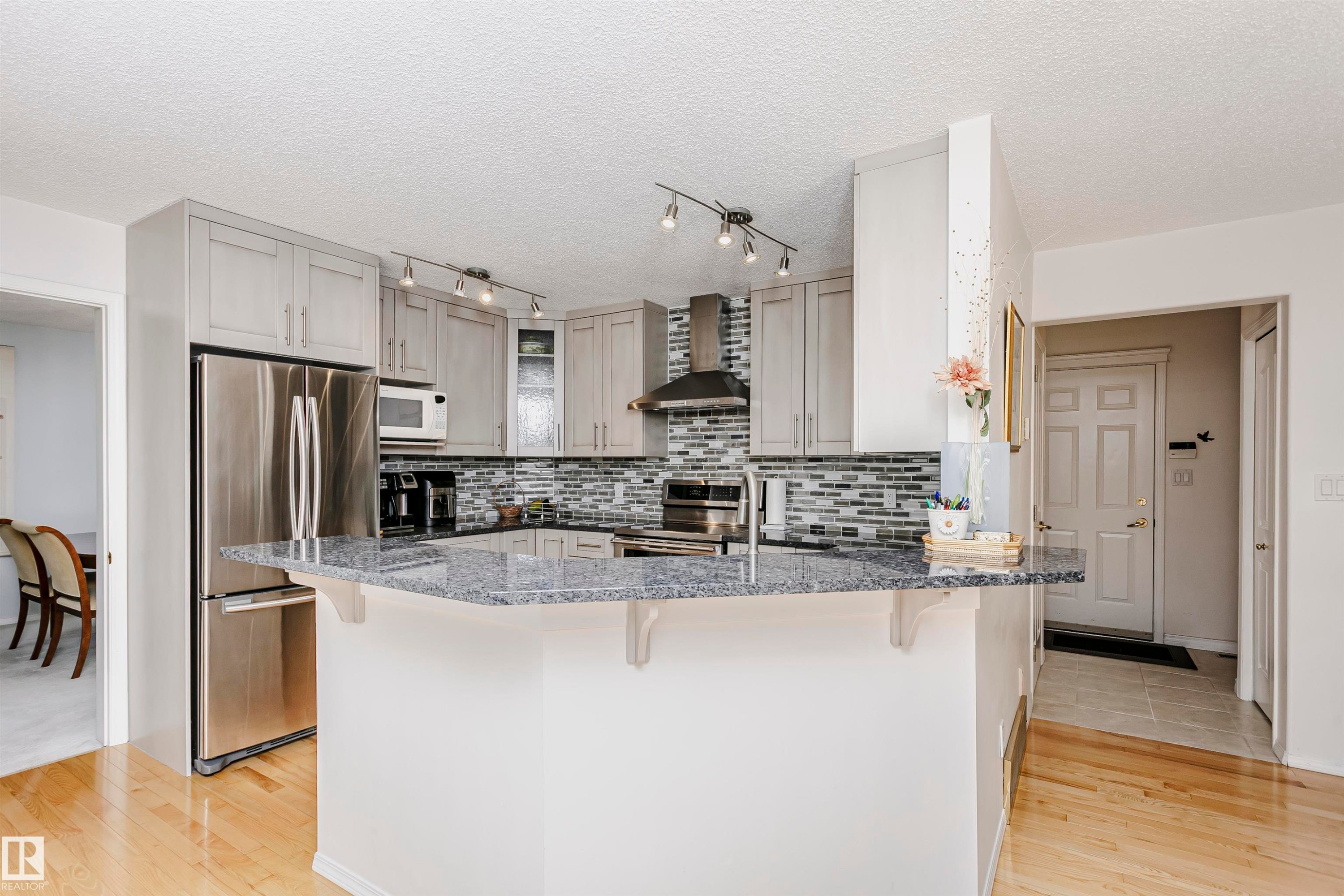 Kitchen featuring light gray cabinetry with brushed nickel hardware, a multi-tone tile backsplash, granite-finish countertops, stainless steel appliances, and track lighting - 11023 11A Avenue Nw, Edmonton, AB - Indoor Photo Showing Kitchen With Upgraded Kitchen
