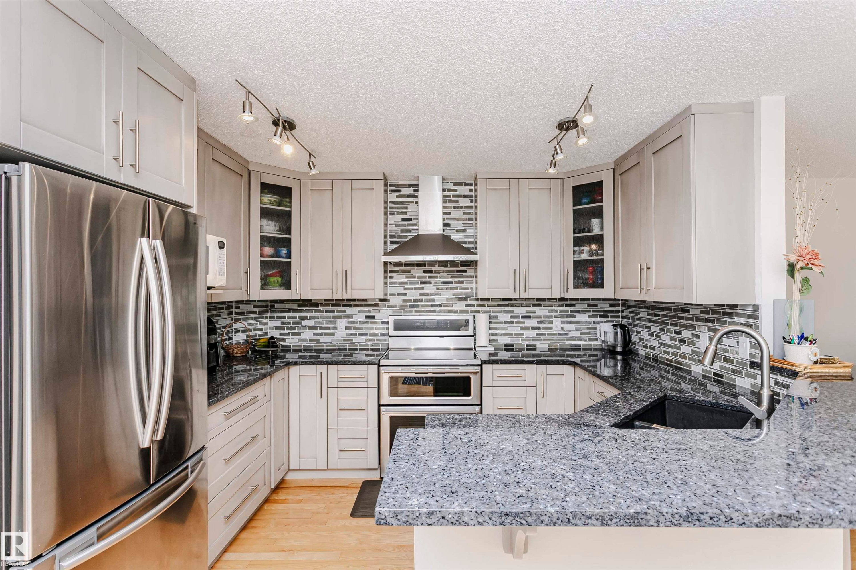 Contemporary kitchen featuring stainless steel appliances, light wood-finish cabinetry, a striking mosaic tile backsplash, and speckled granite countertops with an undermount sink - 11023 11A Avenue Nw, Edmonton, AB - Indoor Photo Showing Kitchen With Upgraded Kitchen