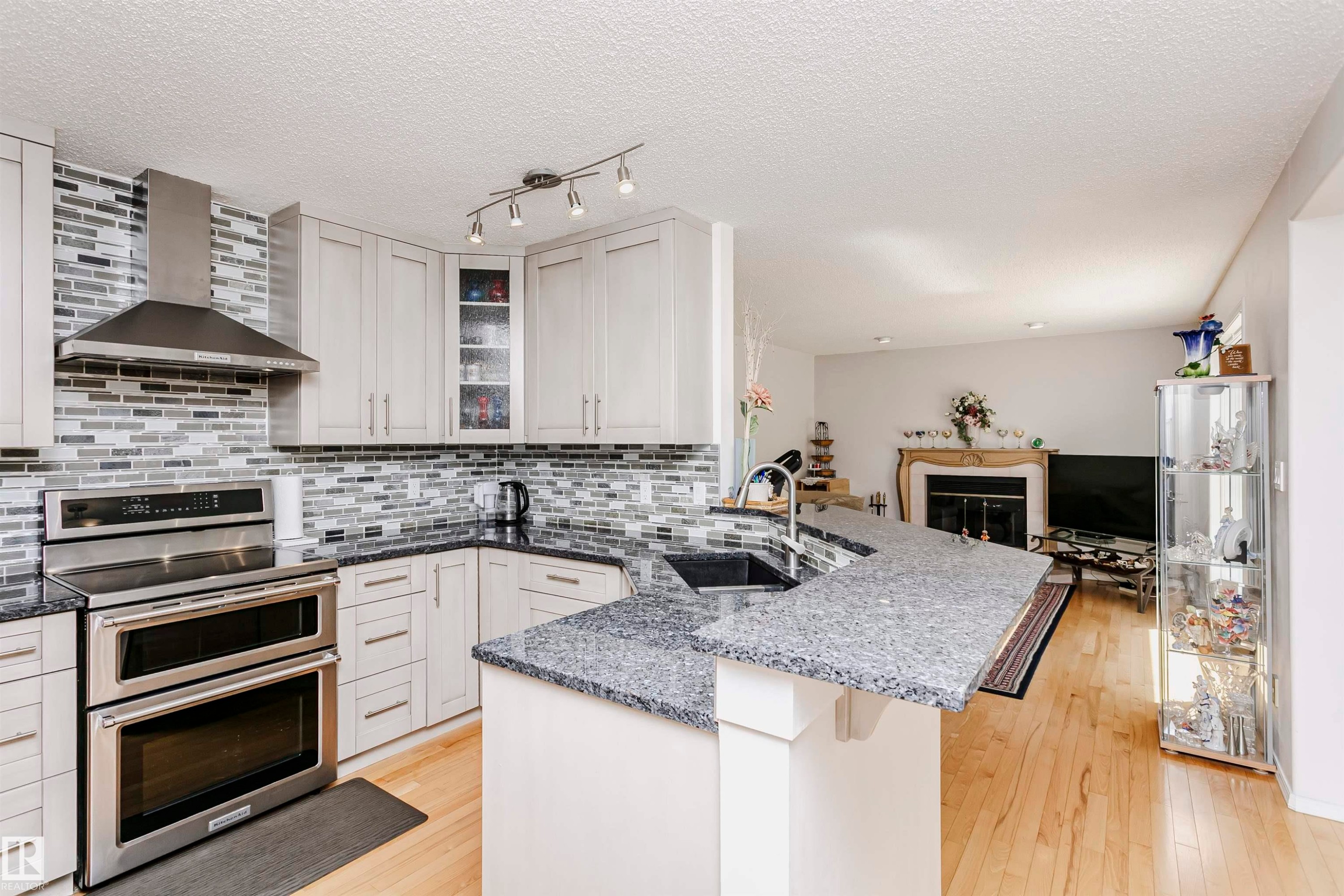 Modern kitchen with stainless steel appliances, mosaic tile backsplash, light wood-finish flooring, and a stone countertop peninsula - 11023 11A Avenue Nw, Edmonton, AB - Indoor Photo Showing Kitchen With Upgraded Kitchen