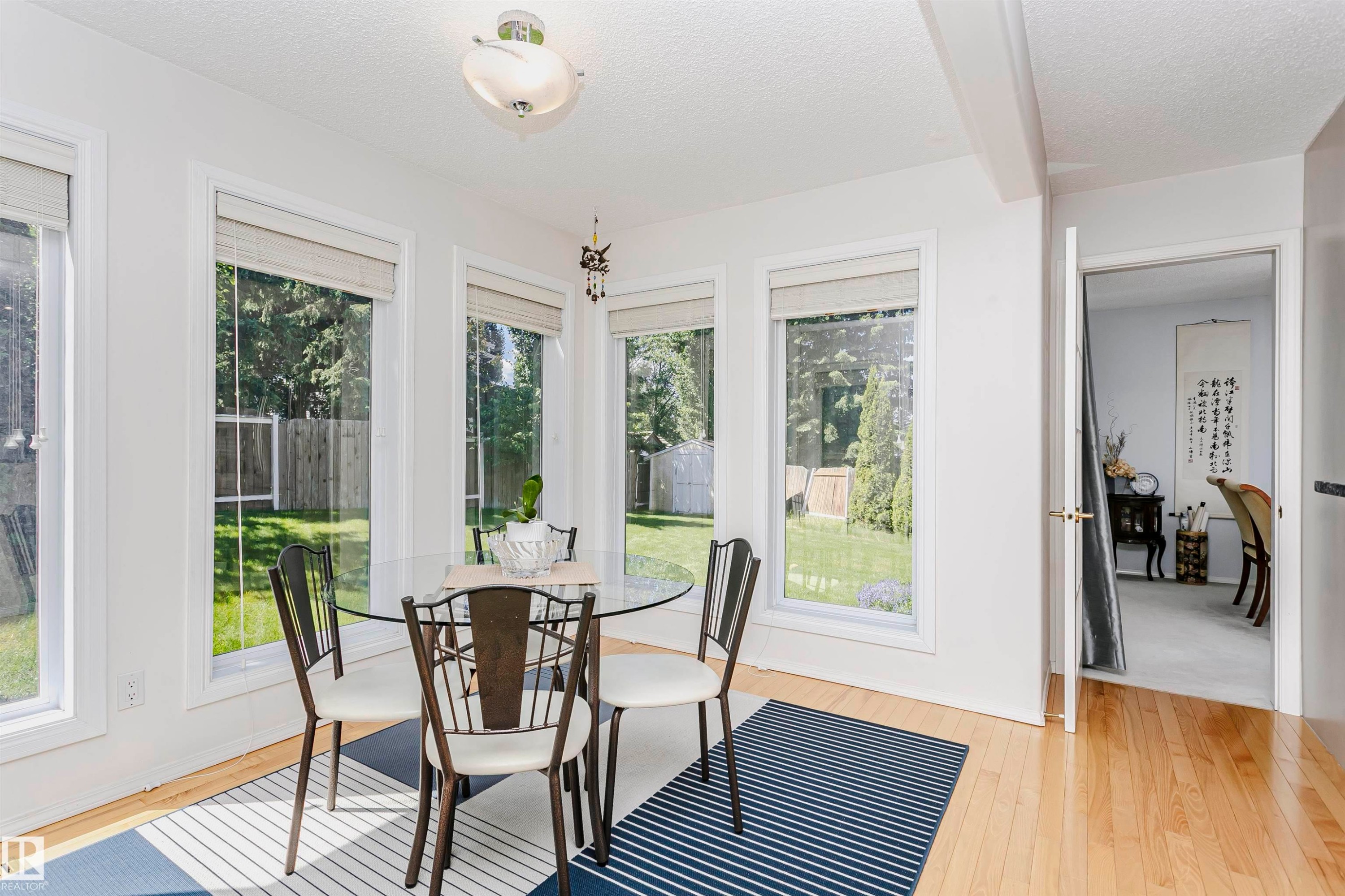 Dining area featuring multiple large windows, wood-finish flooring, a contemporary ceiling light fixture, and a doorway opening to another room - 11023 11A Avenue Nw, Edmonton, AB - Indoor
