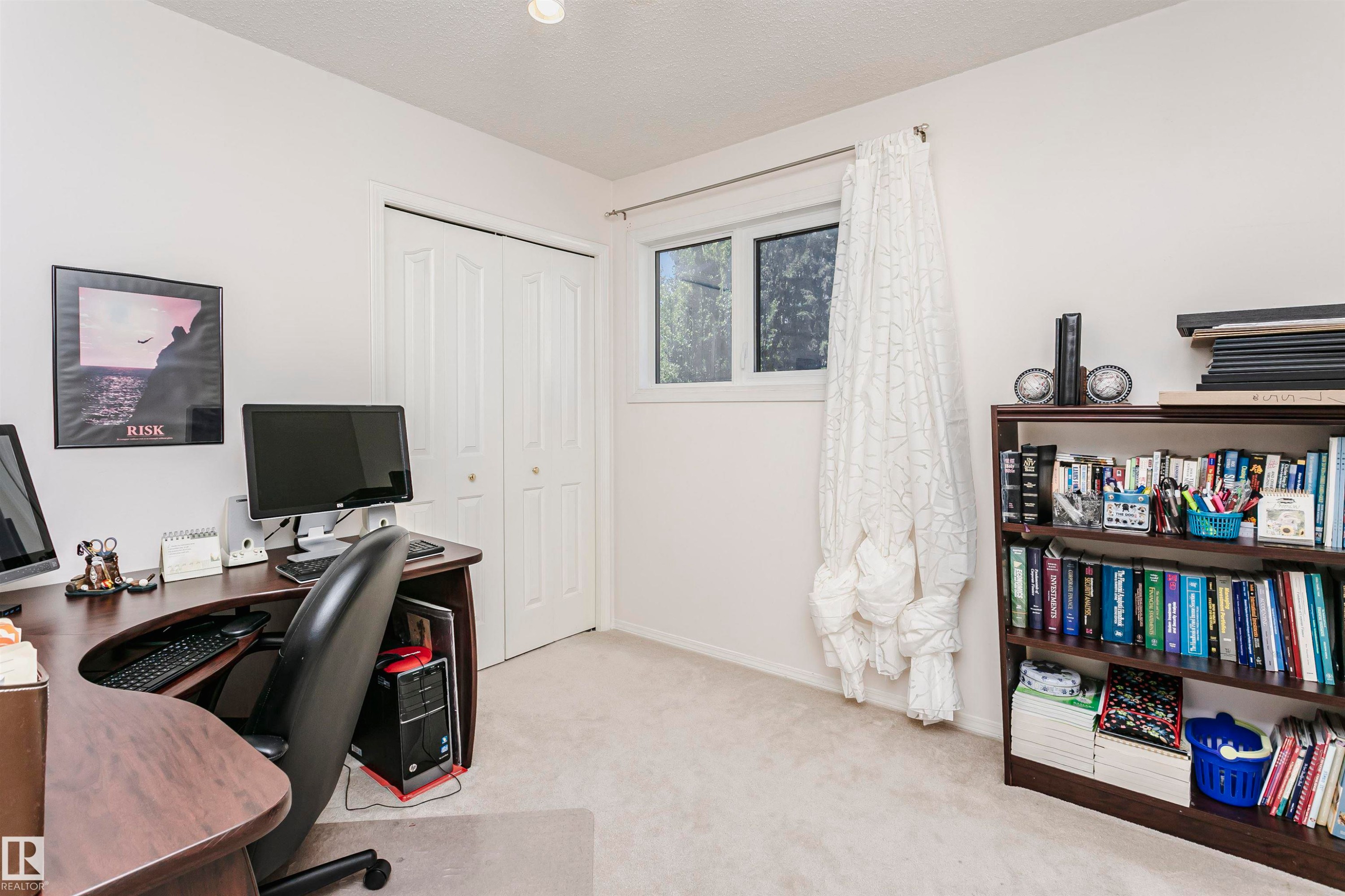 White wall finish with neutral carpeting, featuring a window with white trim, a built-in closet with bifold doors, and a built-in wooden bookcase - 11023 11A Avenue Nw, Edmonton, AB - Indoor Photo Showing Office