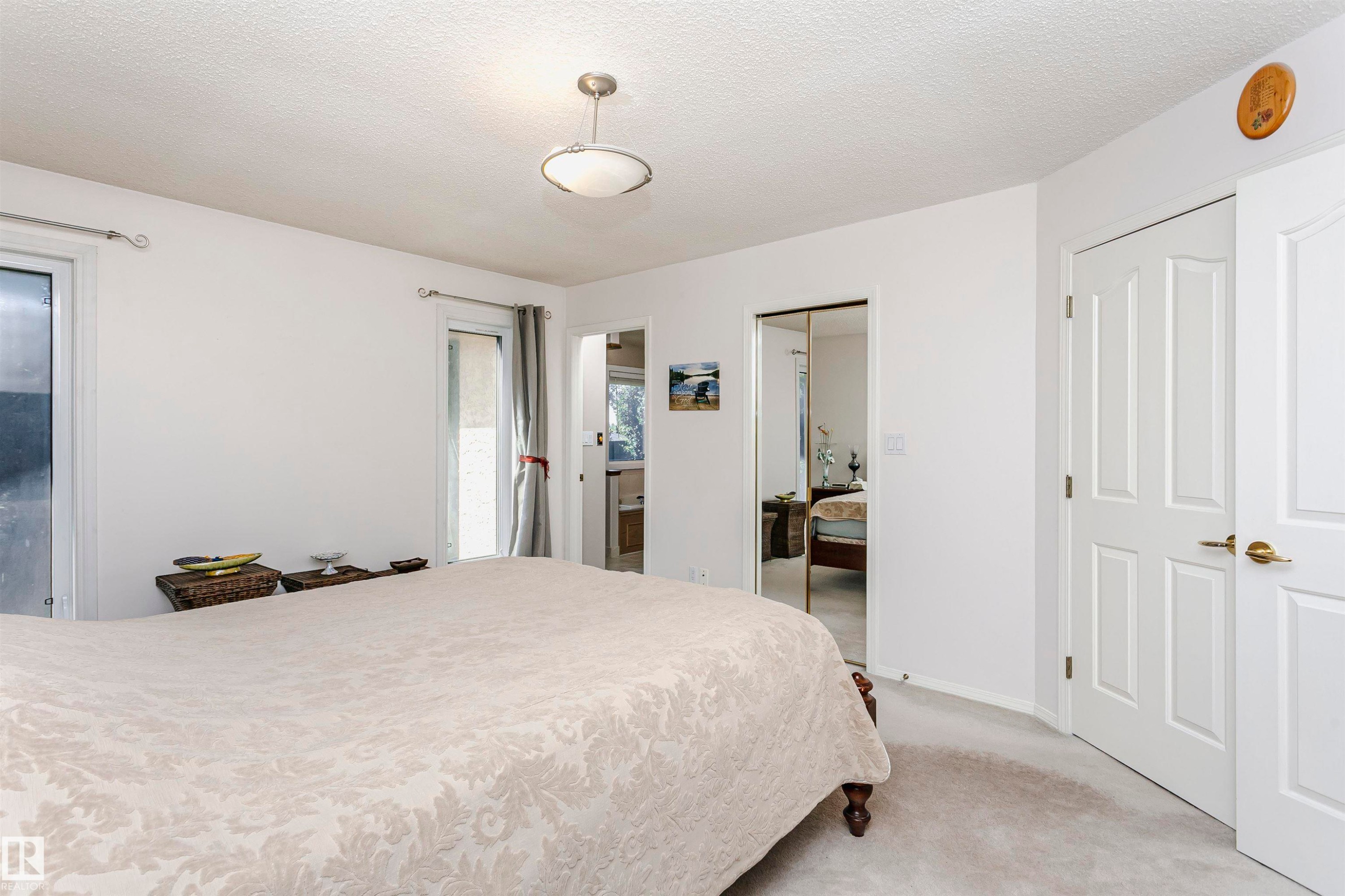 Carpeted room with a ceiling-mounted light fixture, two white panel doors with brass hardware, and a mirrored sliding closet door - 11023 11A Avenue Nw, Edmonton, AB - Indoor Photo Showing Bedroom