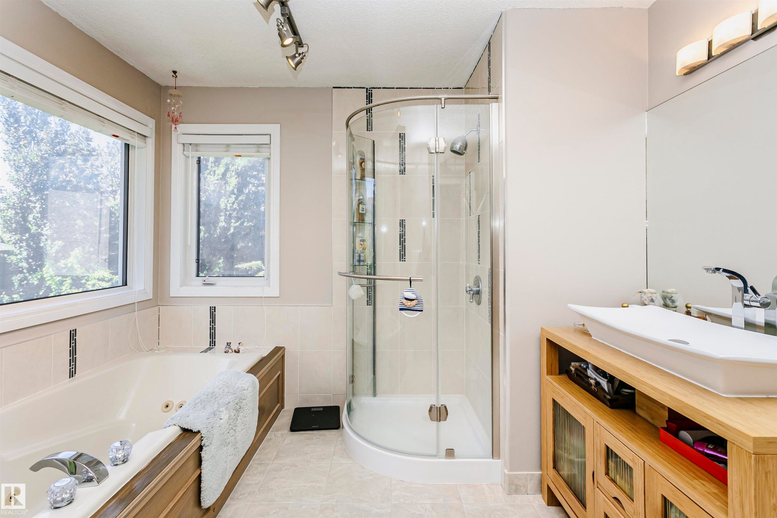 Freestanding soaking tub with wood-finish paneling, a glass-enclosed shower, wood-finish vanity with vessel sink, and large mirror - 11023 11A Avenue Nw, Edmonton, AB - Indoor Photo Showing Bathroom