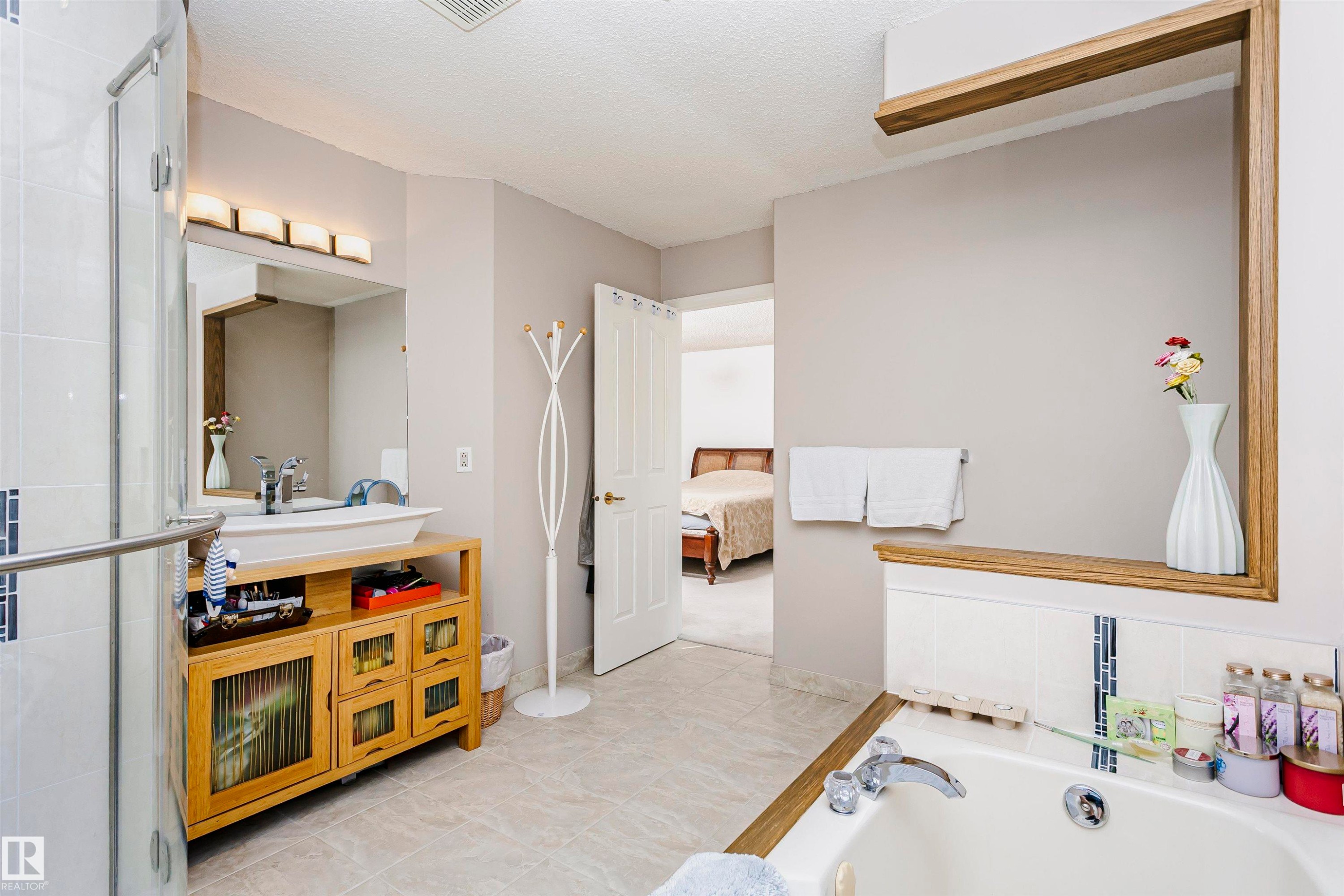 Bathroom featuring a soaker tub with tile surround, glass-enclosed shower, a wood-finish vanity with vessel sink, and an integrated wood-frame shelving unit - 11023 11A Avenue Nw, Edmonton, AB - Indoor Photo Showing Bathroom