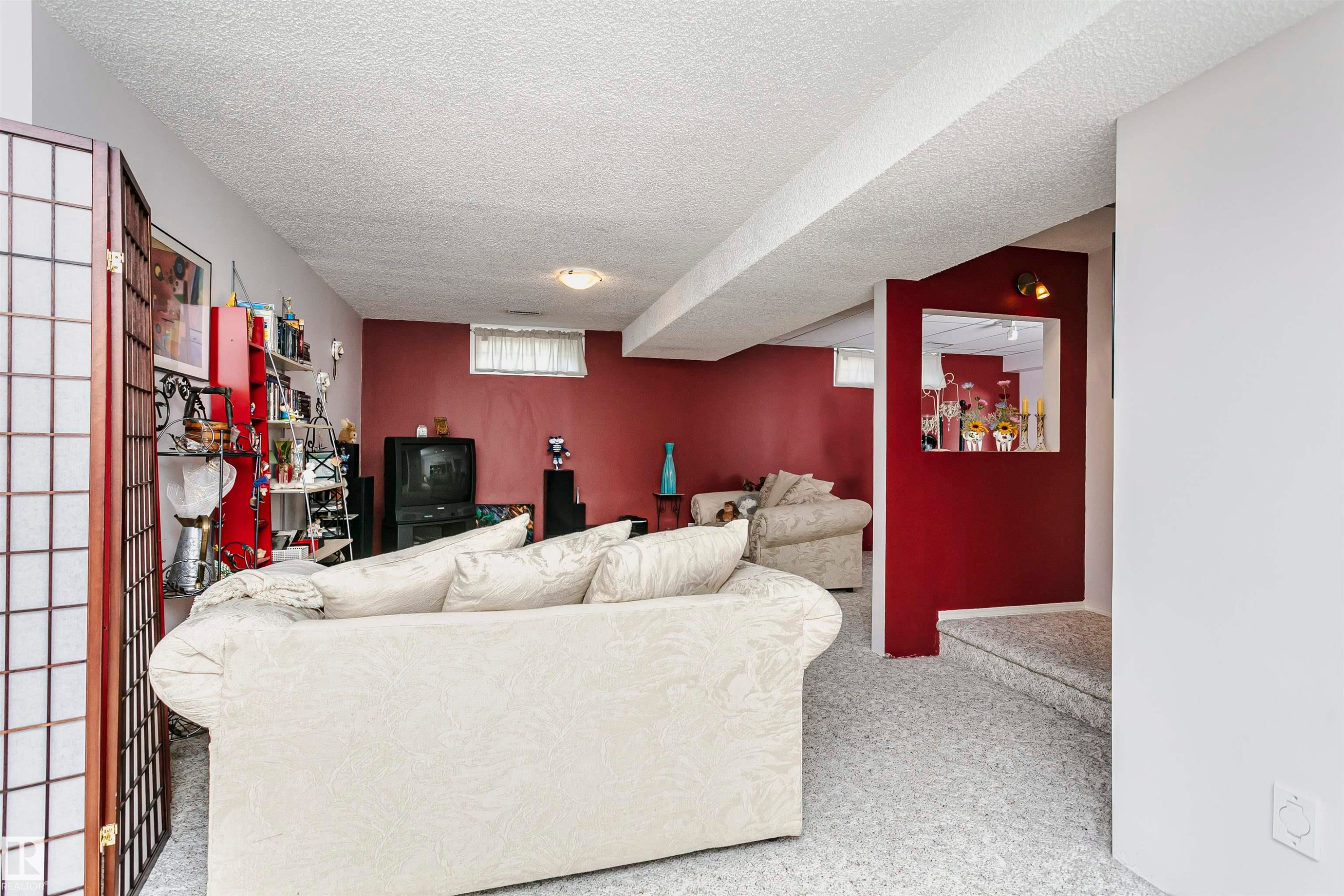 Lower level recreation room with red accent wall and light gray carpet - 11023 11A Avenue Nw, Edmonton, AB - Indoor
