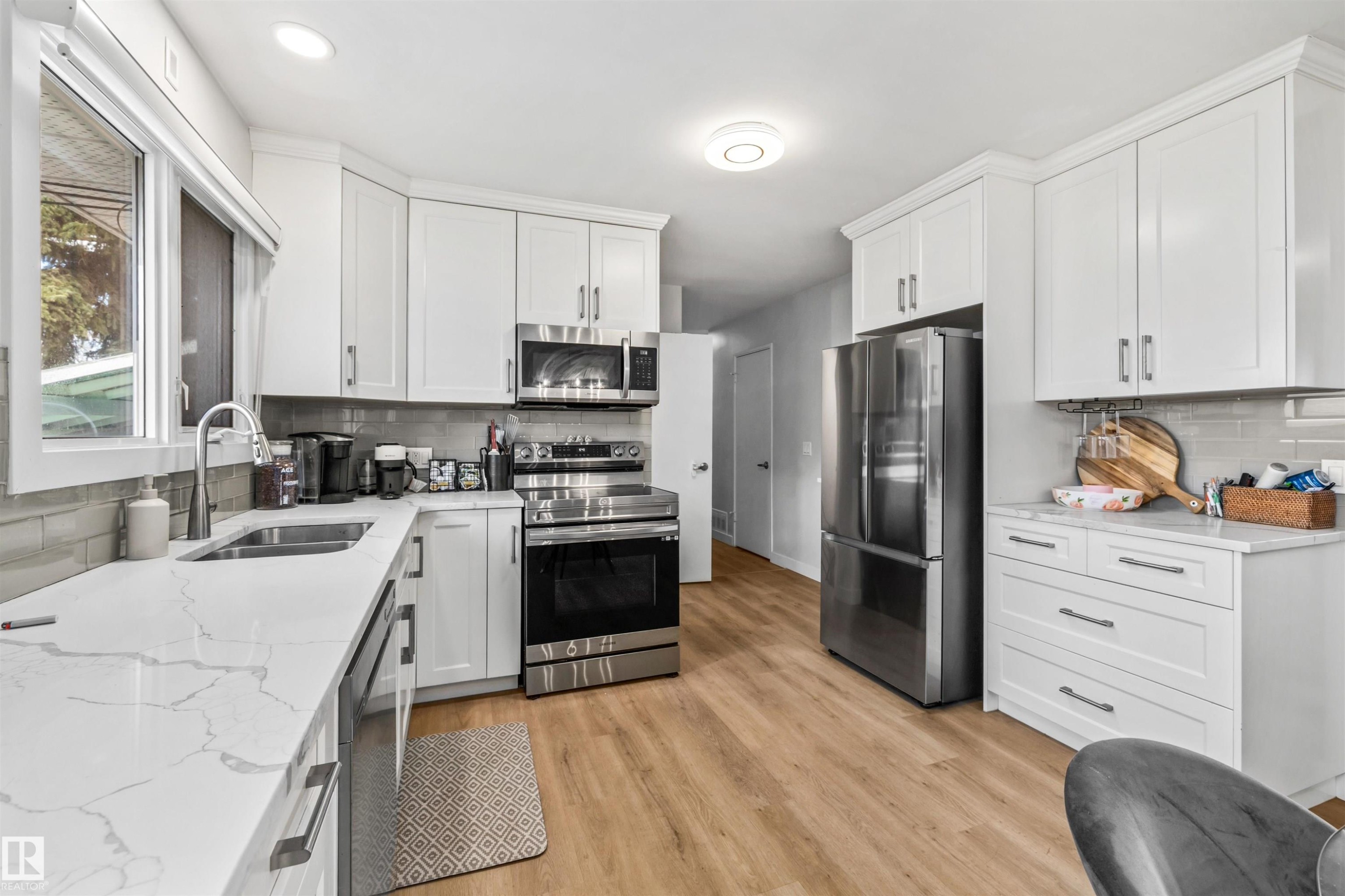 Modern kitchen featuring white shaker cabinetry, stainless steel appliances, marble-look countertops, a light gray tile backsplash, and light wood-finish flooring - 10130 62 Street, Edmonton, AB - Indoor Photo Showing Kitchen With Double Sink With Upgraded Kitchen