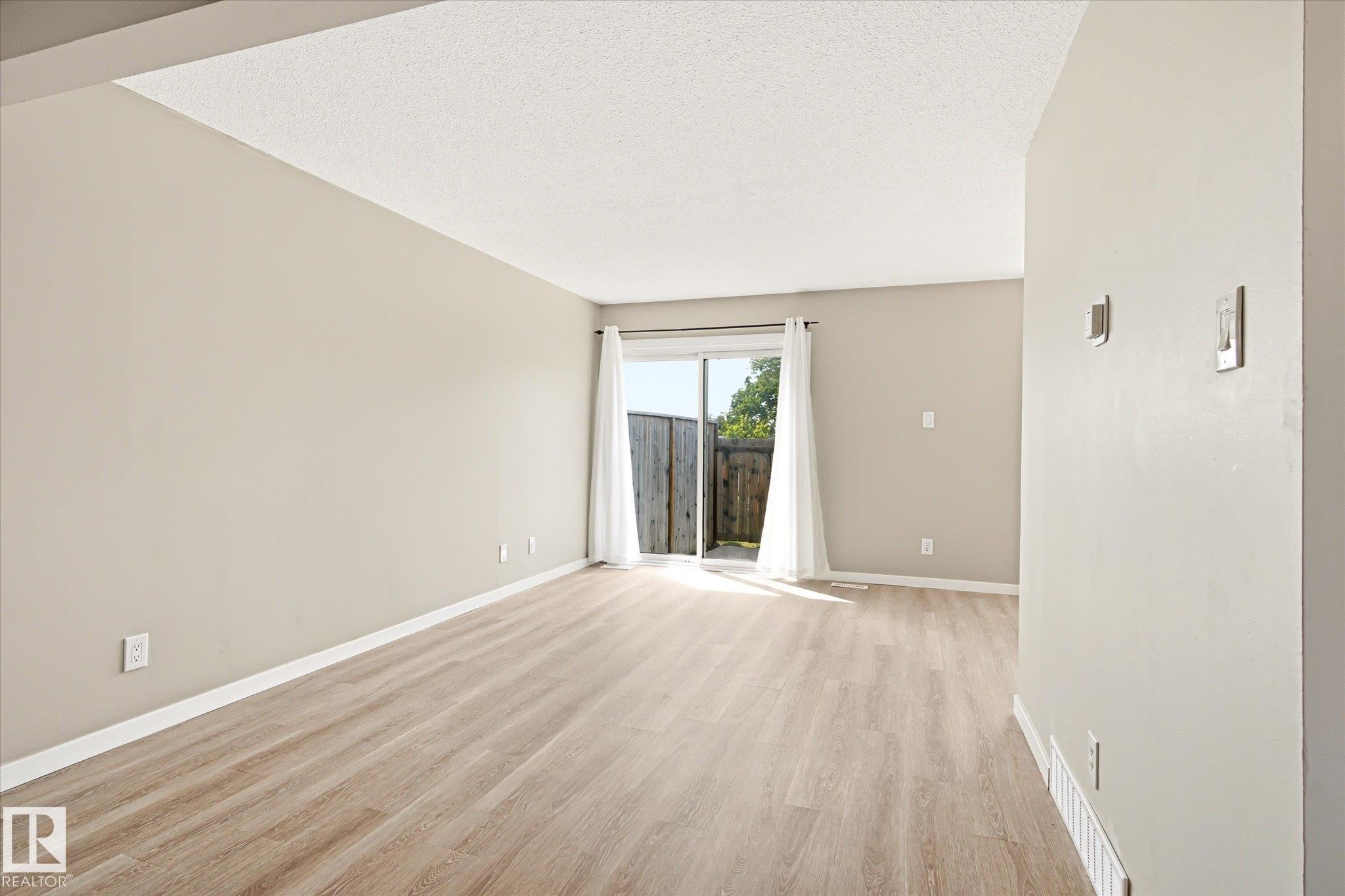 Spacious room featuring light wood-finish flooring, neutral wall tones, and a sliding glass door leading to an outdoor area - 186 Cornell Crest, Edmonton, AB