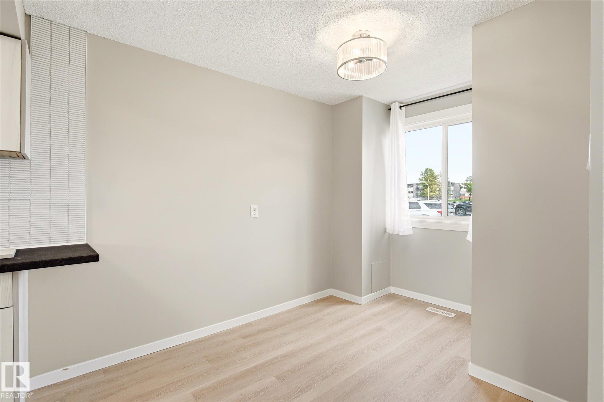 Naturally lit interior space featuring light wood-finish flooring, a contemporary semi-flush mount ceiling fixture, and a window with white trim - 186 Cornell Crest, Edmonton, AB
