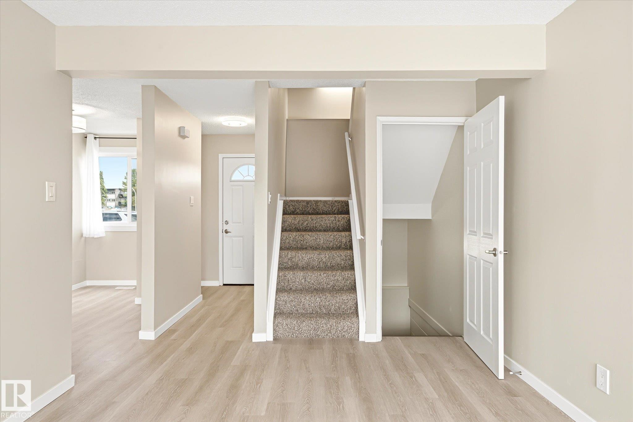 Foyer featuring light wood-finish flooring, a carpeted staircase with white railing, and a white paneled door with hardware - 186 Cornell Crest, Edmonton, AB