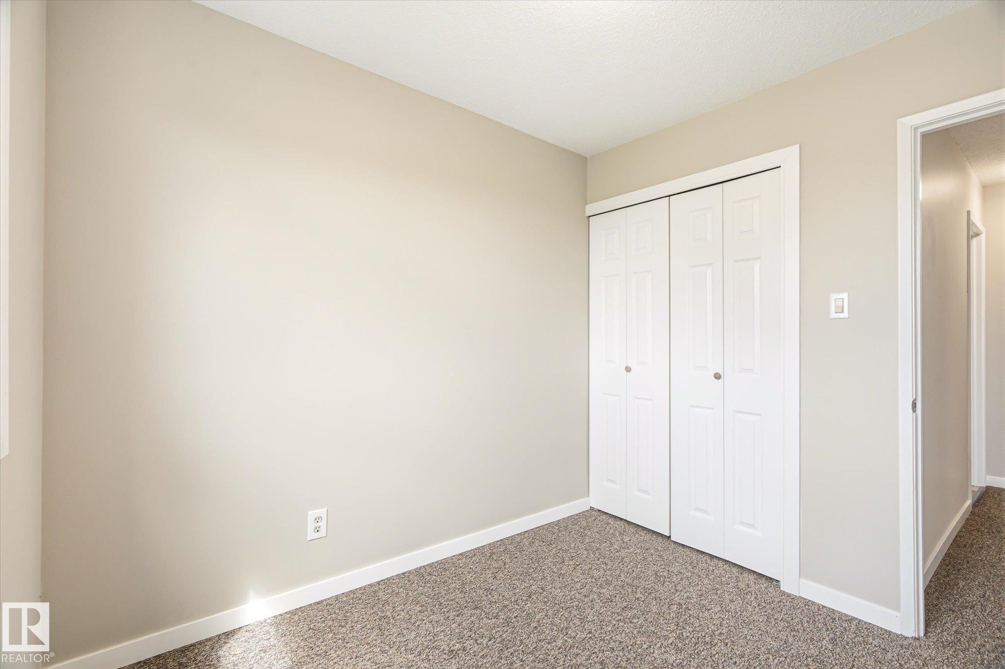 Room featuring light neutral wall paint, white trim, textured carpet, and bi-fold closet doors - 186 Cornell Crest, Edmonton, AB