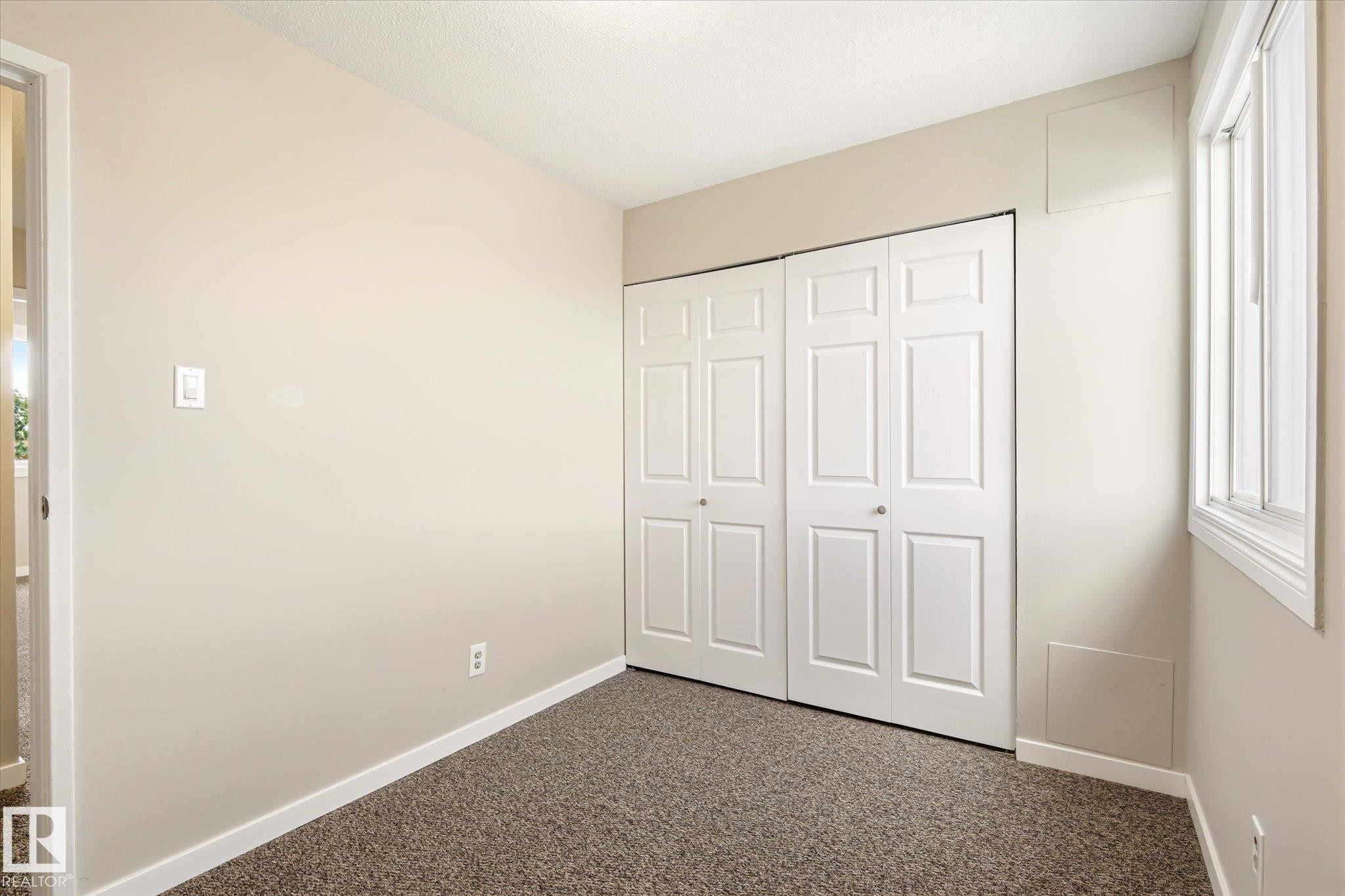 Neutral-toned room featuring a window, bi-fold closet doors, wall-to-wall carpeting, and white baseboards - 186 Cornell Crest, Edmonton, AB