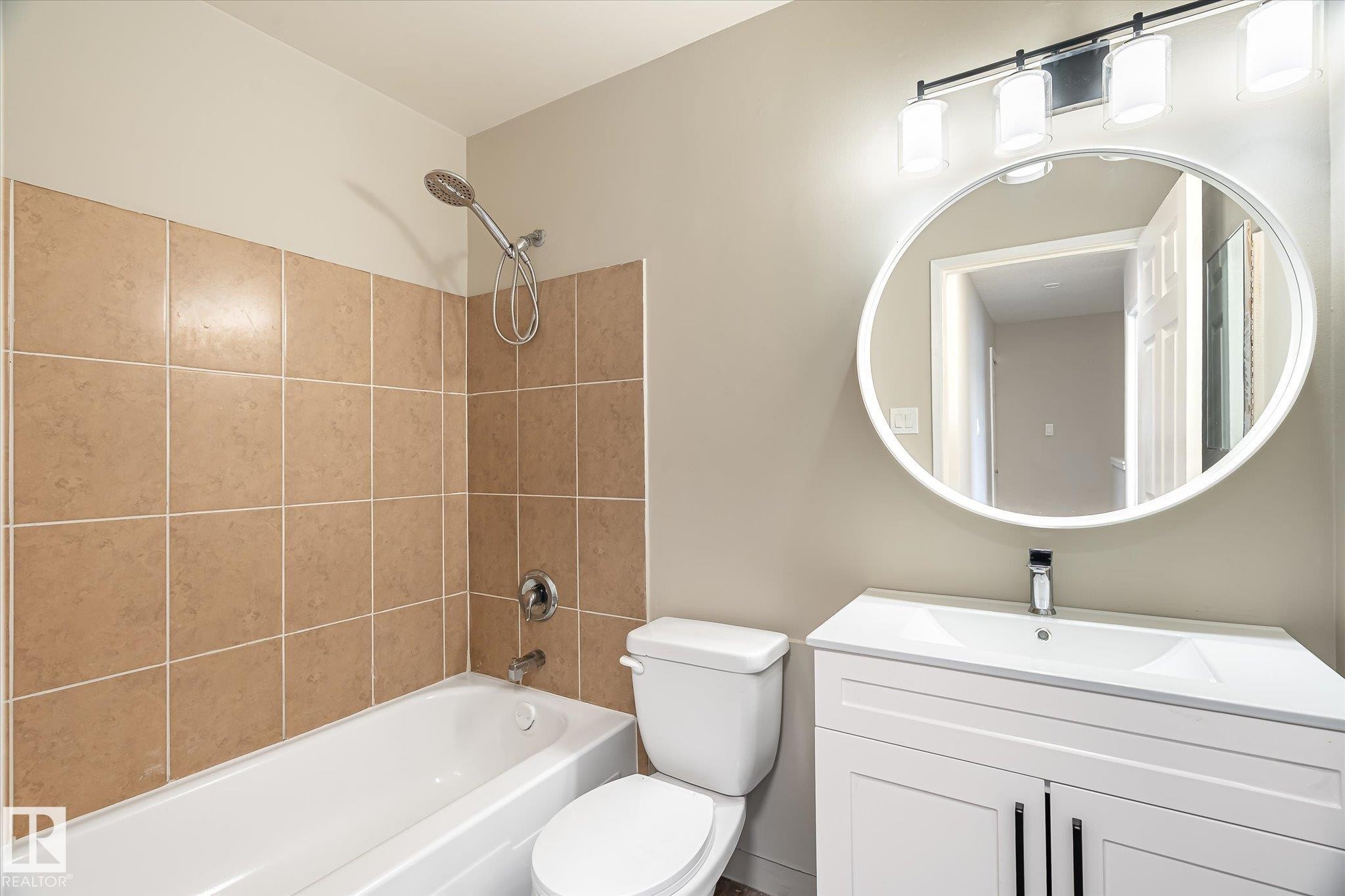 Bathroom featuring a white vanity with integrated sink, chrome faucet, and contemporary oval mirror - 186 Cornell Crest, Edmonton, AB