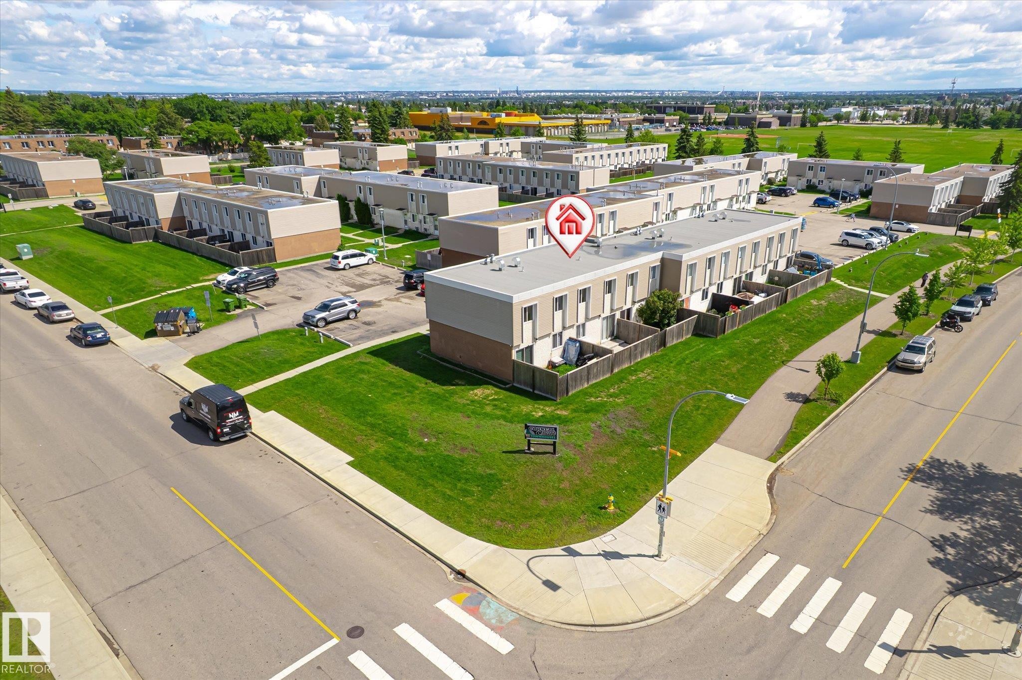 Townhome community featuring multi-level units with private fenced yards, communal green spaces, surface parking, and concrete sidewalks - 186 Cornell Crest, Edmonton, AB
