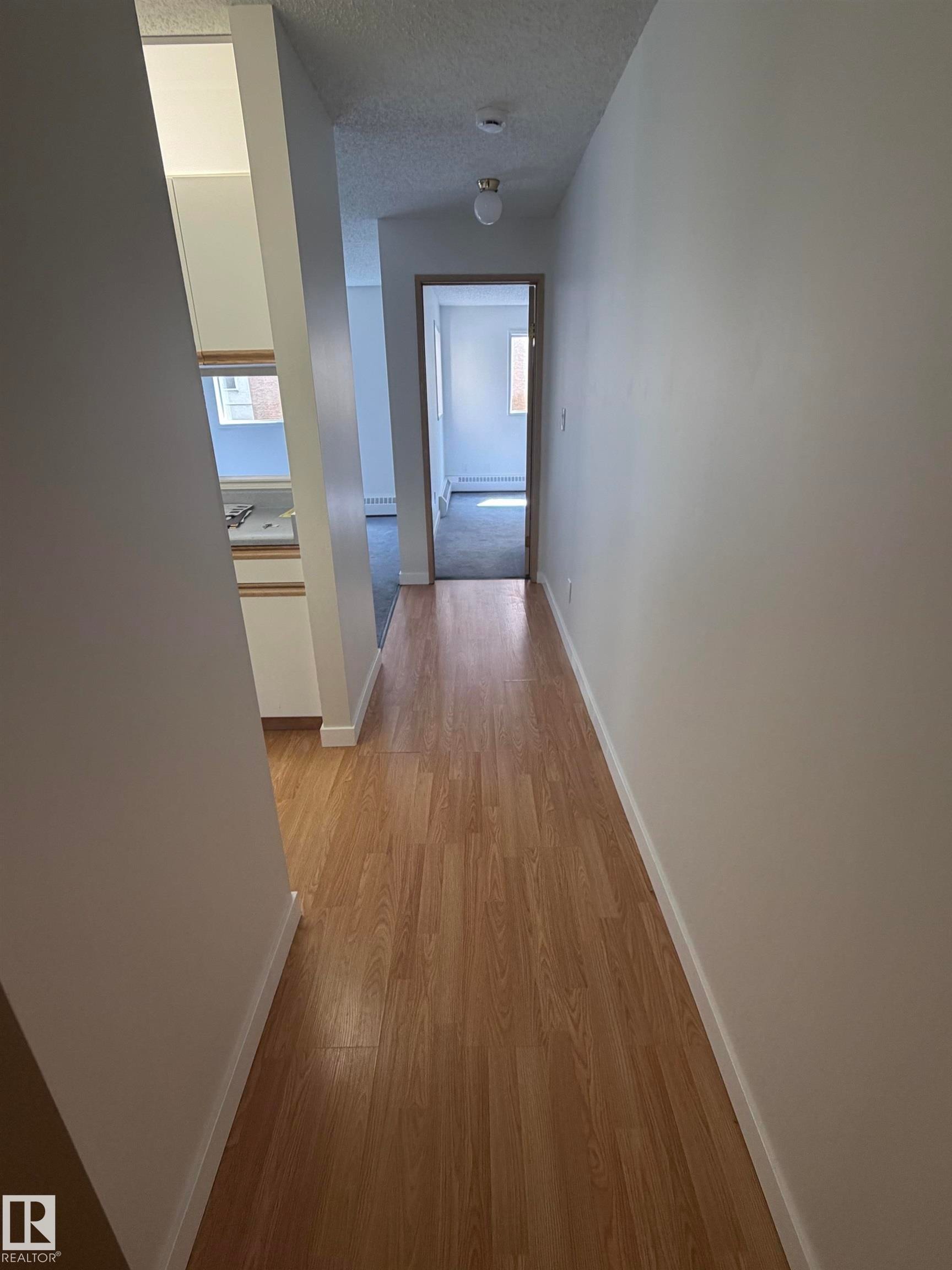 Hallway featuring wood-finish flooring, white baseboards, and neutral wall paint - 213 17467 98A Avenue, Edmonton, AB