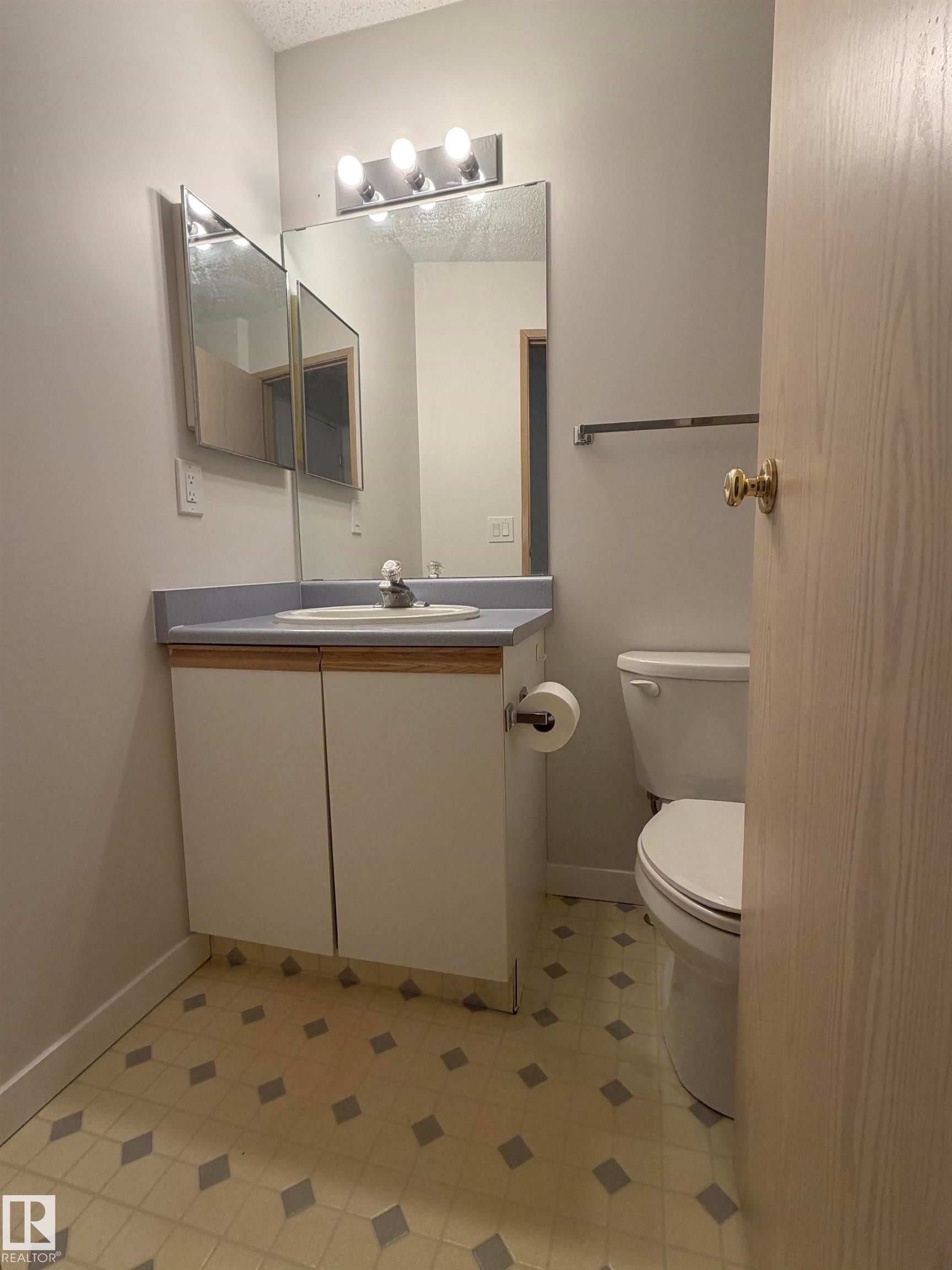 Bathroom featuring a vanity with an integrated sink, a large wall mirror, and overhead strip lighting - 213 17467 98A Avenue, Edmonton, AB