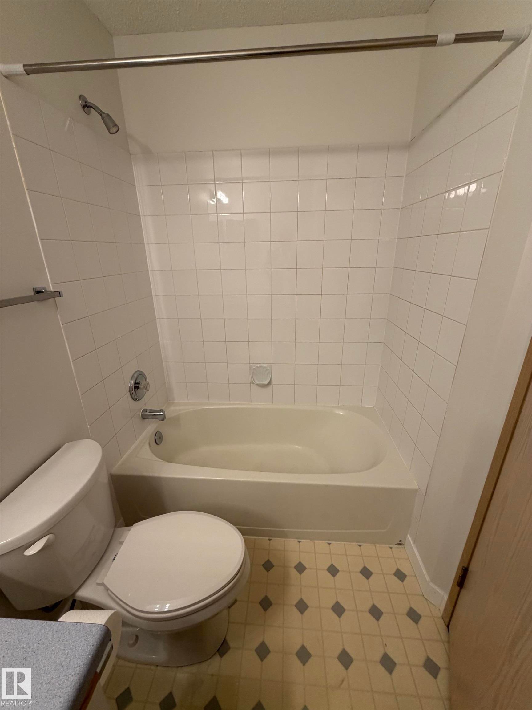 Bathroom featuring a bathtub with an integrated shower, white subway tile surround, chrome fixtures, and patterned vinyl flooring - 213 17467 98A Avenue, Edmonton, AB