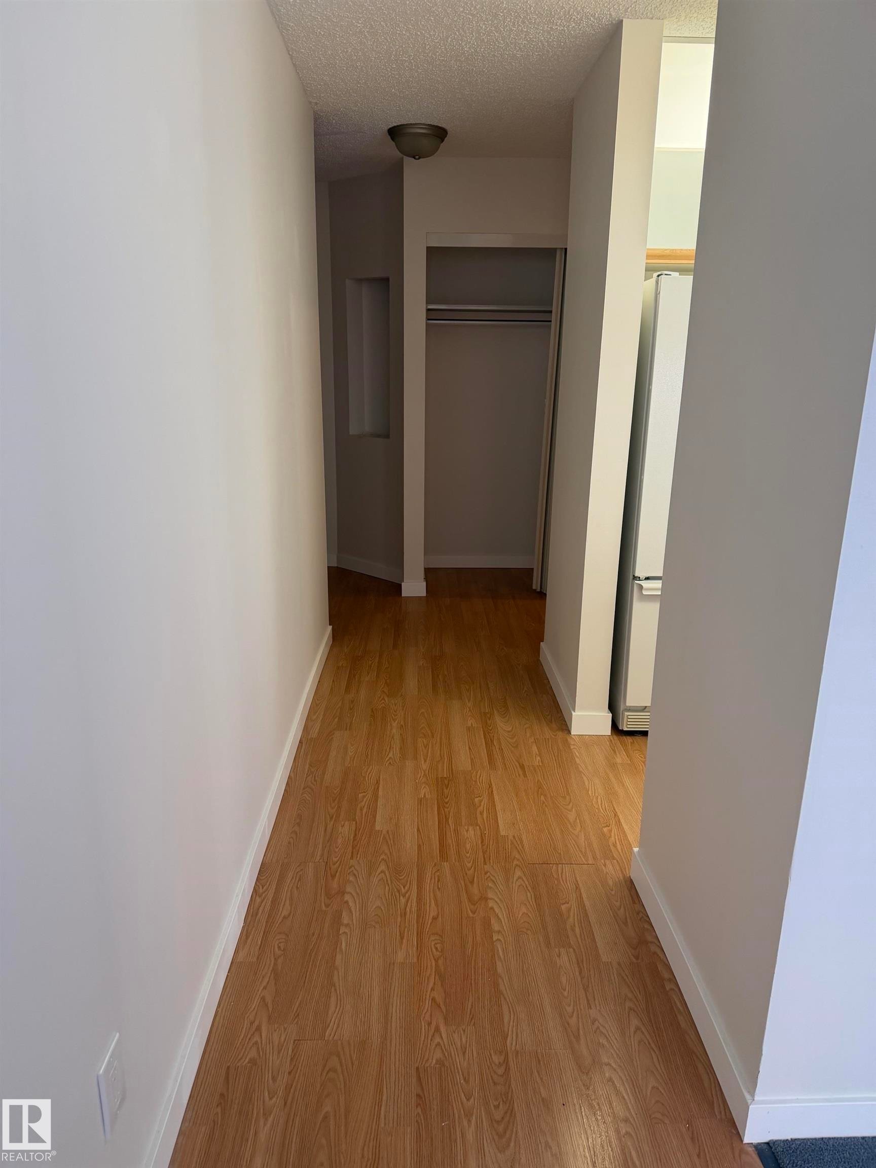 Hallway featuring wood-finish flooring, white walls, and white baseboards - 213 17467 98A Avenue, Edmonton, AB