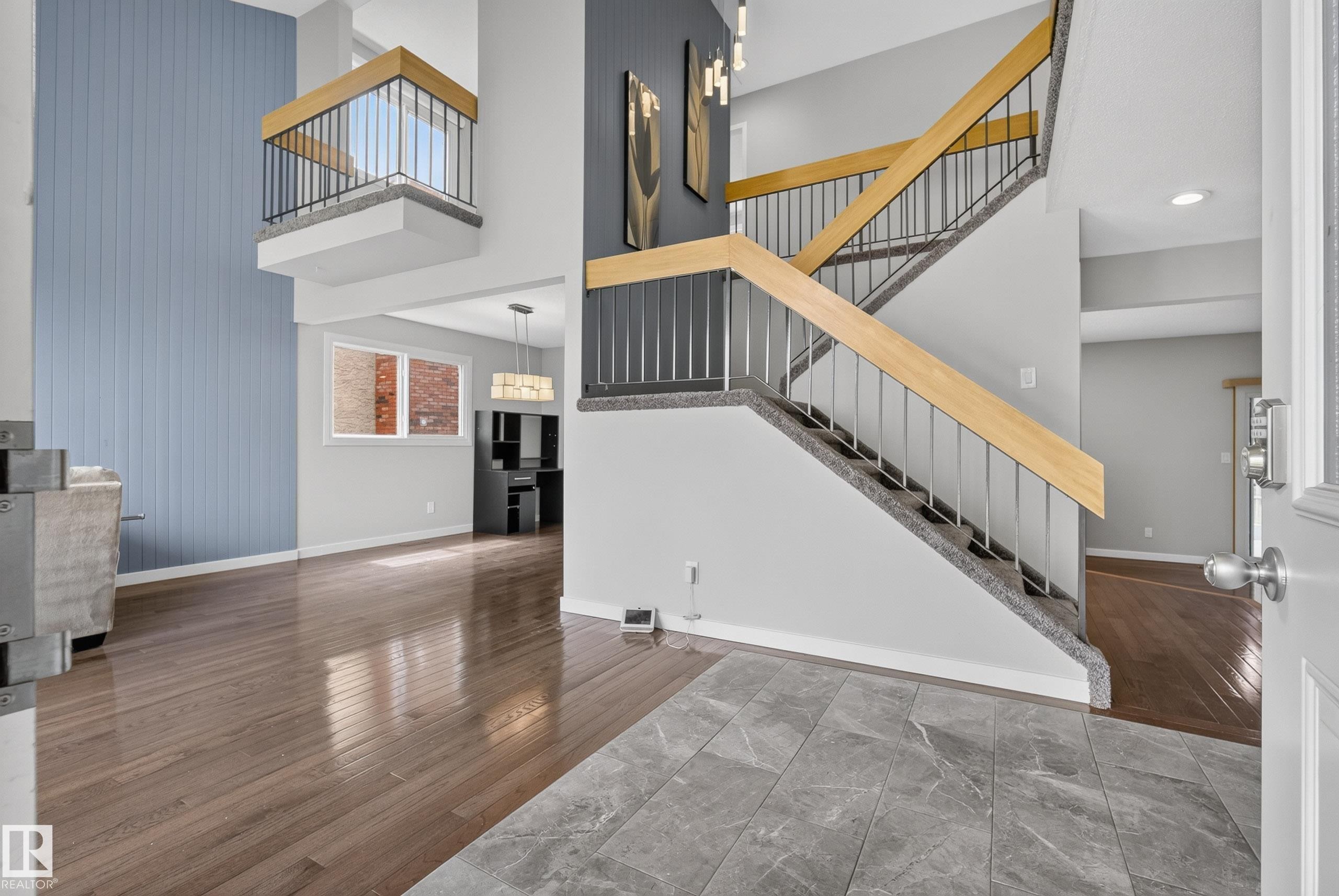 Two-story foyer featuring a grand staircase with wood-finish handrails and metal balusters, a second-story balcony overlook, and a paneled accent wall - 2712 104 Street, Edmonton, AB