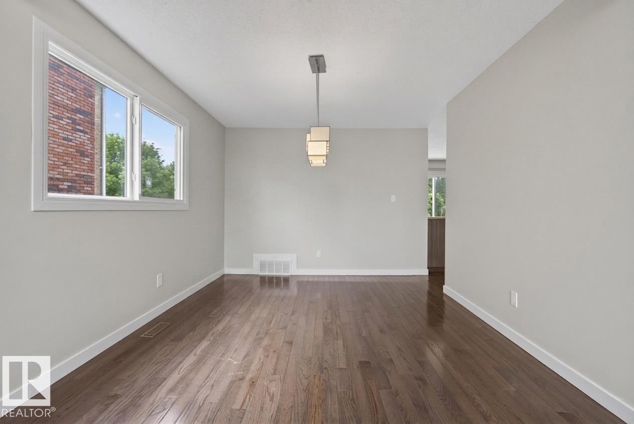 Spacious room featuring wood-finish flooring and a modern linear pendant light fixture - 2712 104 Street, Edmonton, AB