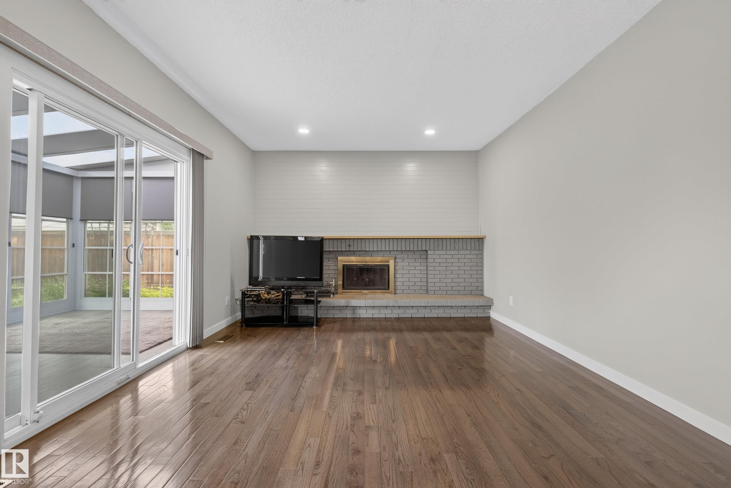 Spacious interior featuring wood-finish flooring and a fireplace with a brick surround - 2712 104 Street, Edmonton, AB