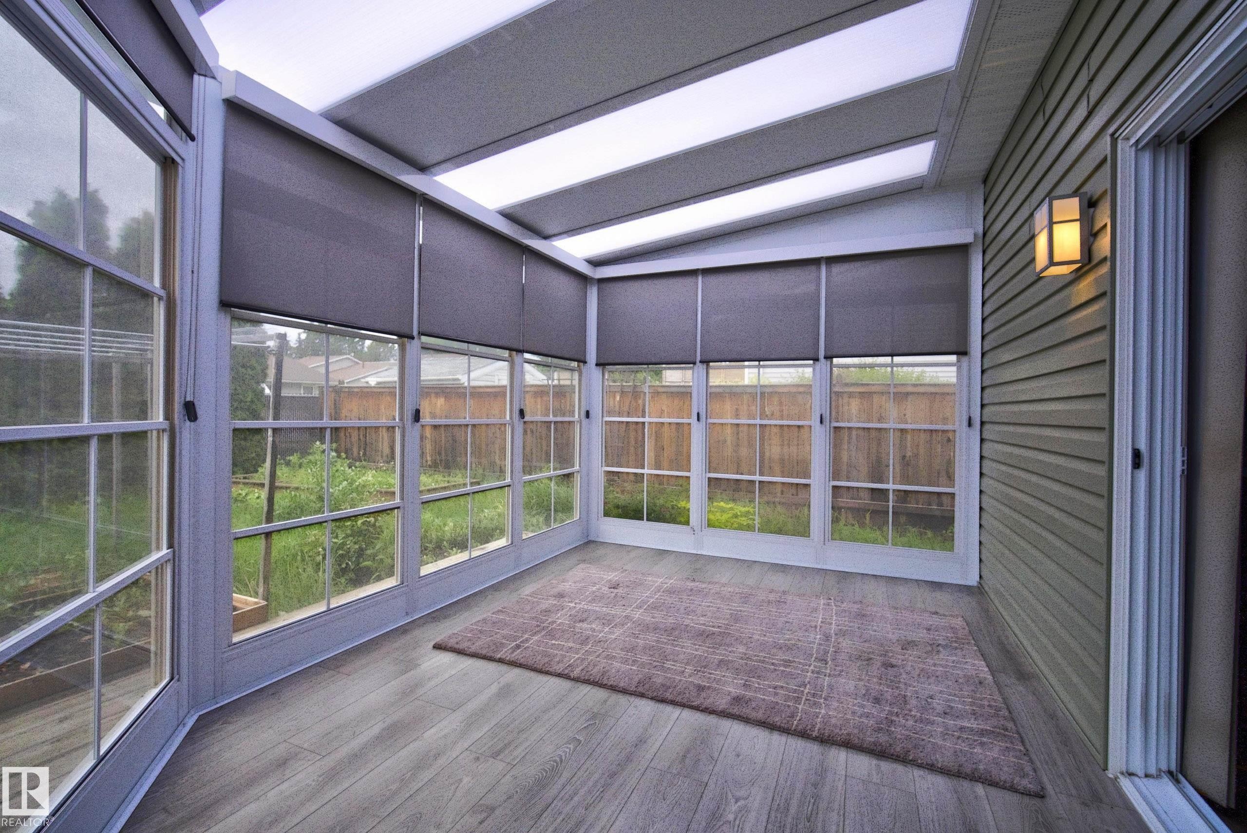 Enclosed sunroom featuring a ceiling with integrated lighting, multiple windows with grid patterns, roller shades, and wood-finish flooring - 2712 104 Street, Edmonton, AB
