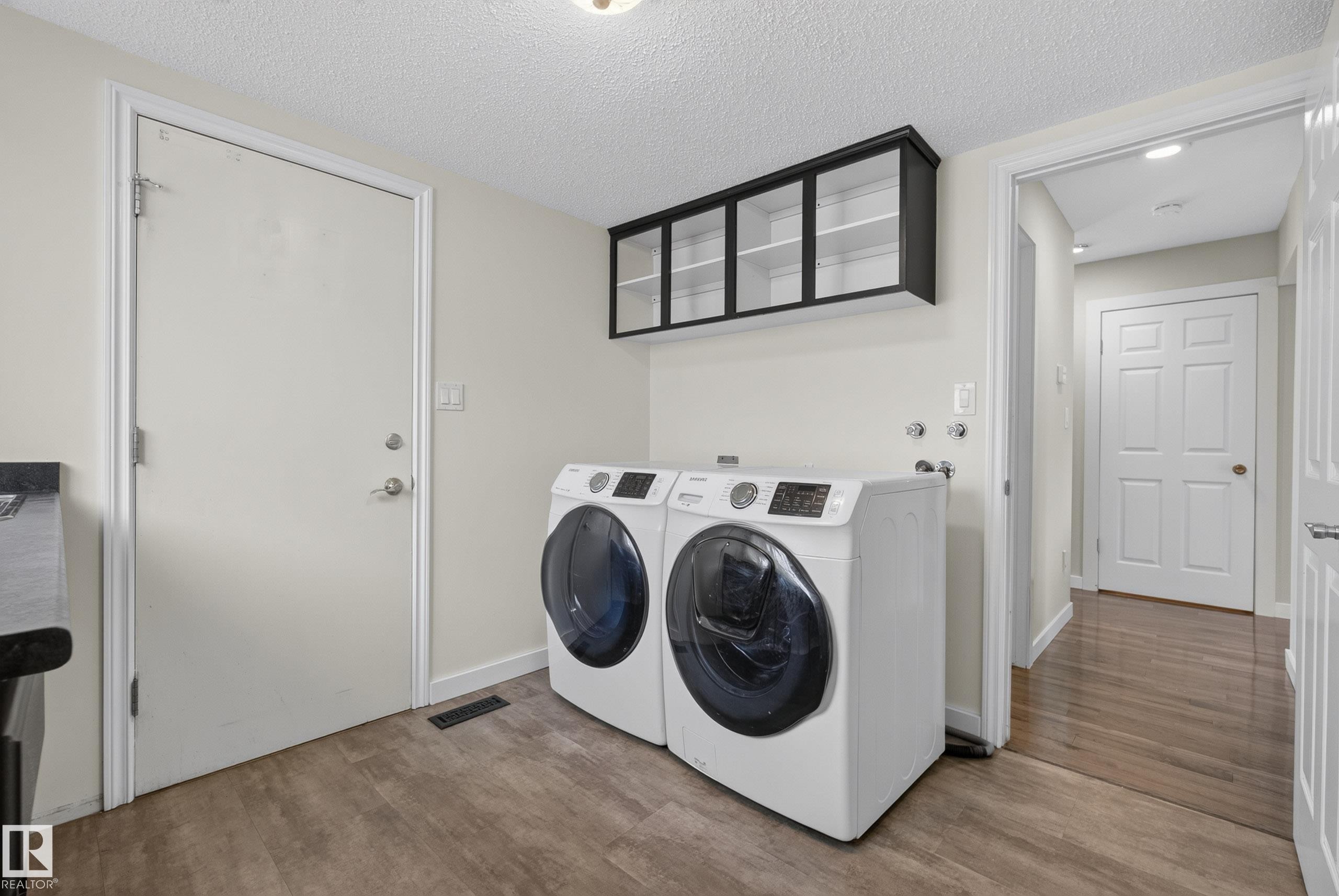 Dedicated laundry area featuring wood-finish flooring and upper cabinetry with clear panel doors - 2712 104 Street, Edmonton, AB