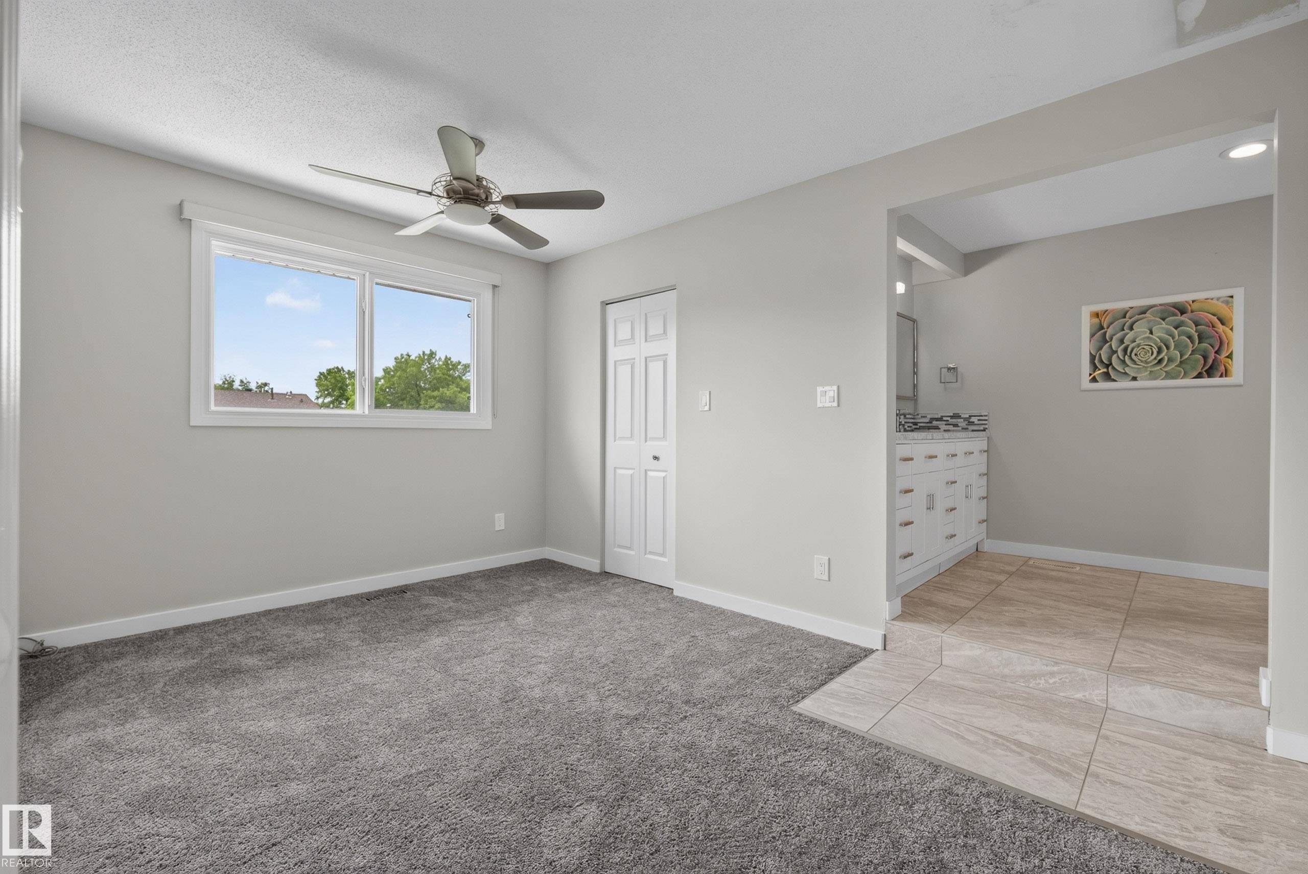 Spacious room with plush gray carpeting, a large window, and a ceiling fan - 2712 104 Street, Edmonton, AB