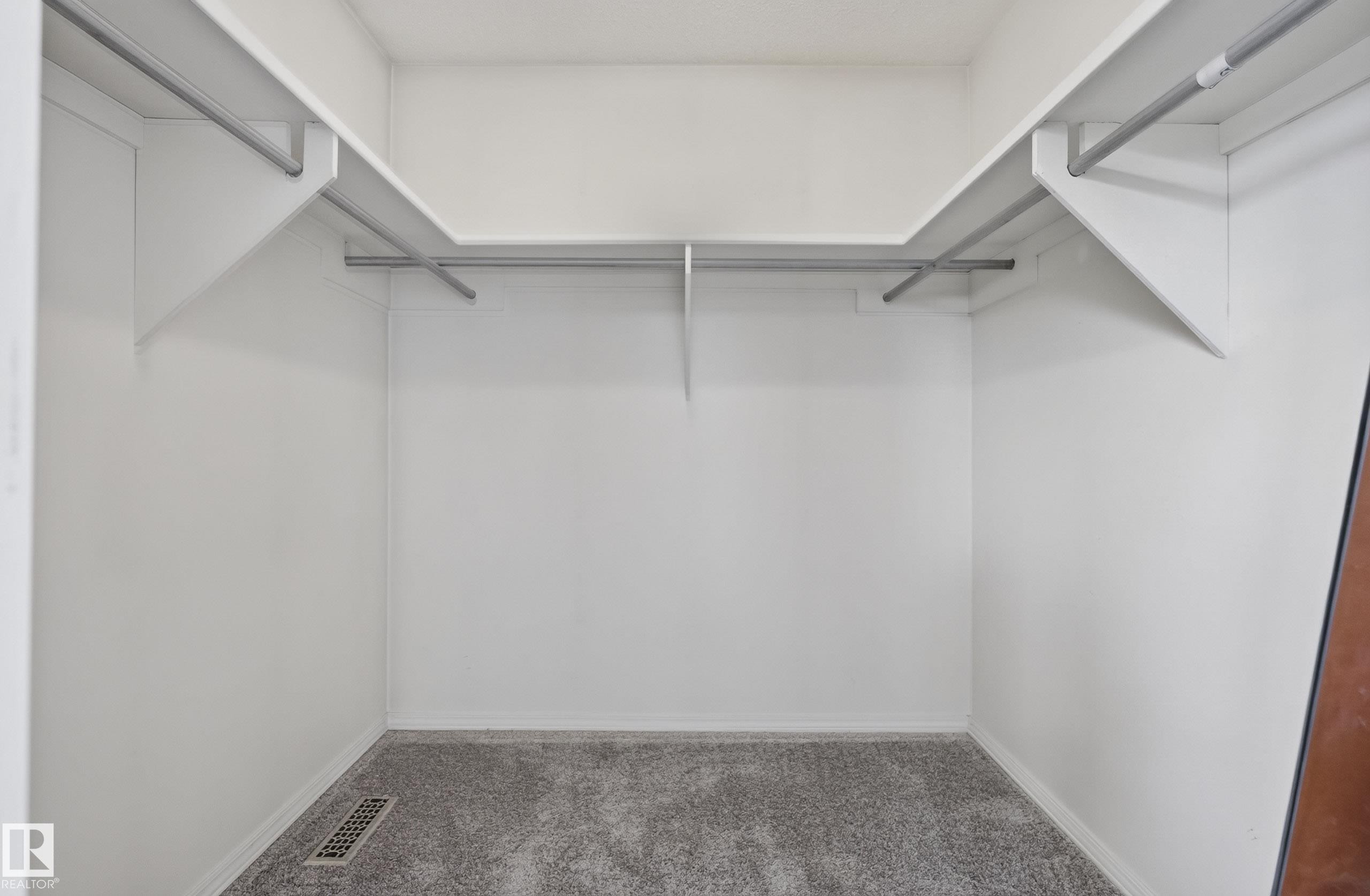 Spacious walk-in closet featuring light grey carpeting, white walls, and built-in shelving with integrated hanging rods - 2712 104 Street, Edmonton, AB