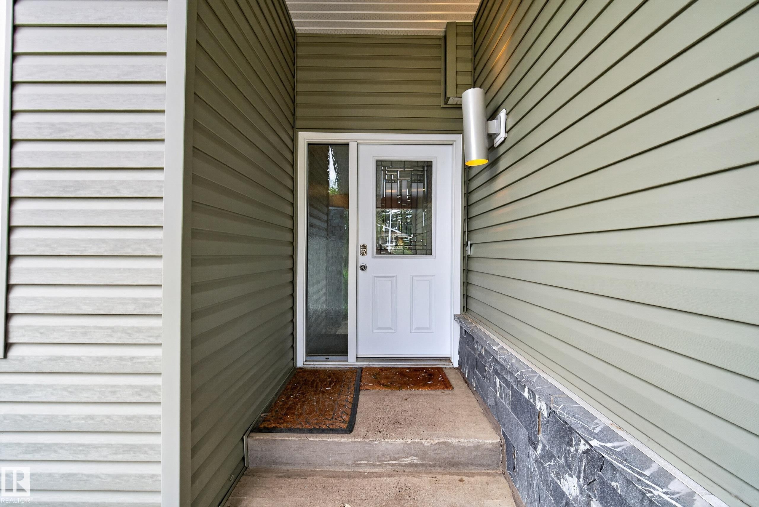 Entryway featuring light green horizontal siding and a white door with decorative glass inserts - 2712 104 Street, Edmonton, AB