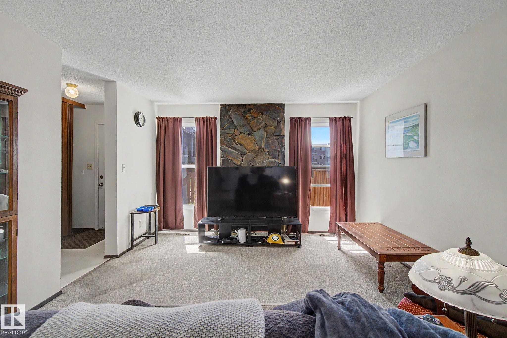 Living area featuring a stone accent wall, light gray carpeting, and white painted walls - 18409 66 Avenue, Edmonton, AB