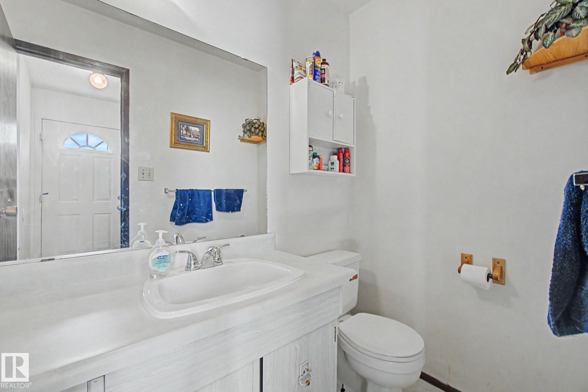 Bathroom featuring a vanity with an integrated sink, a large wall-mounted mirror, and a built-in wall cabinet for storage - 18409 66 Avenue, Edmonton, AB