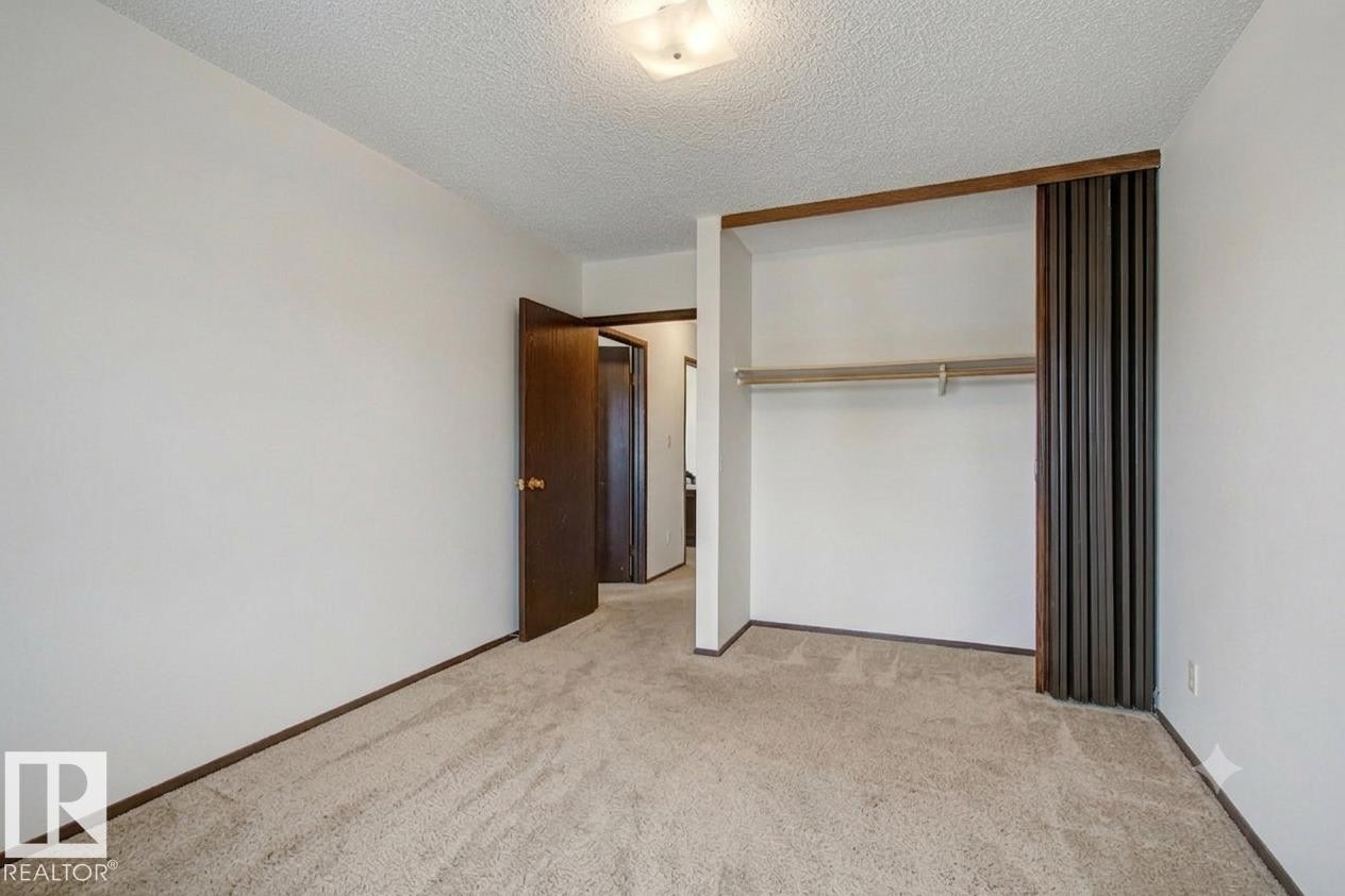 Carpeted room featuring a built-in closet with sliding dark wood doors and an integrated clothing rod - 18409 66 Avenue, Edmonton, AB