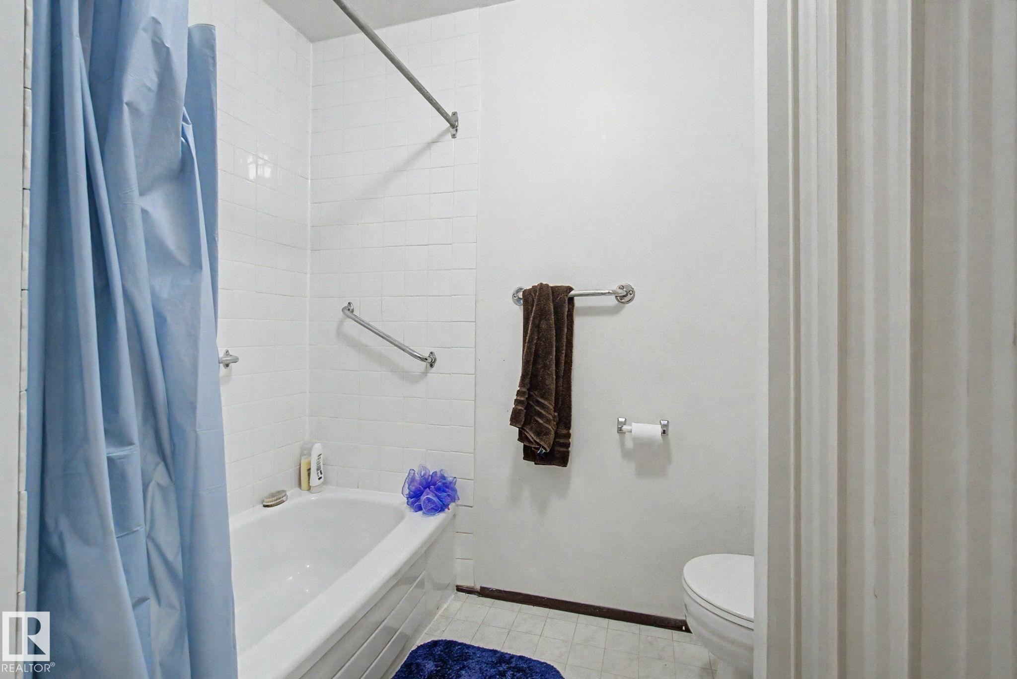 Bathtub with white subway tile surround, chrome grab bars, and a chrome shower rod - 18409 66 Avenue, Edmonton, AB