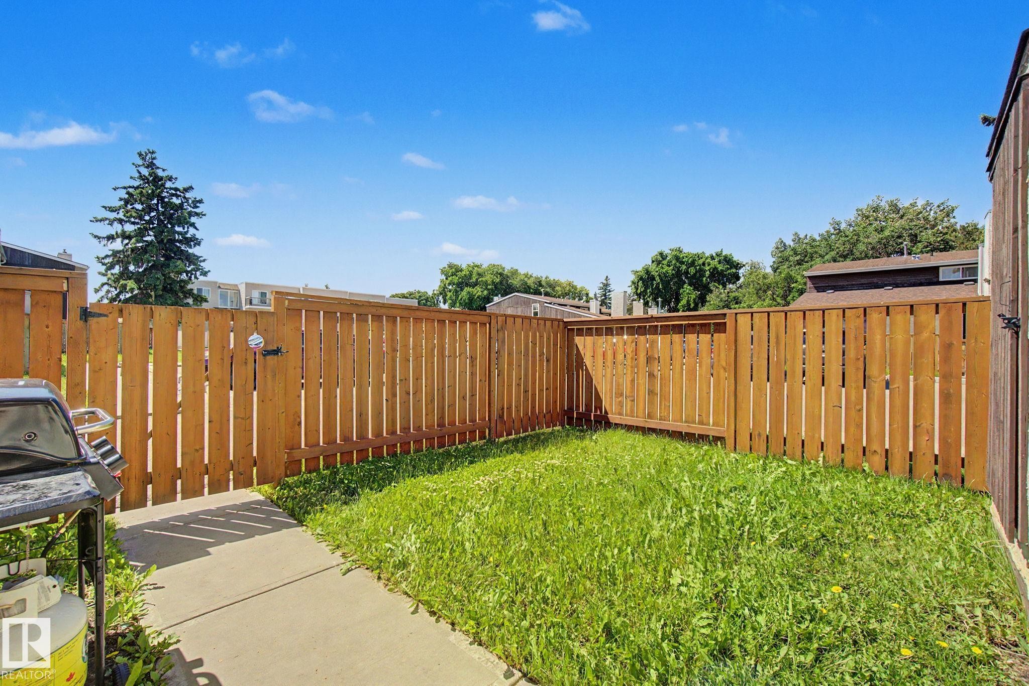 Private backyard featuring a concrete patio, a wooden privacy fence, and a grassy lawn area - 18409 66 Avenue, Edmonton, AB