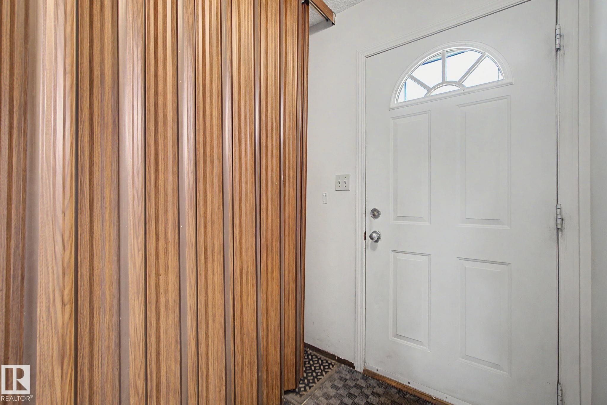 Entryway featuring a white panel door with an arched transom window, wood-finish slatted wall paneling, and checkered flooring - 18409 66 Avenue, Edmonton, AB