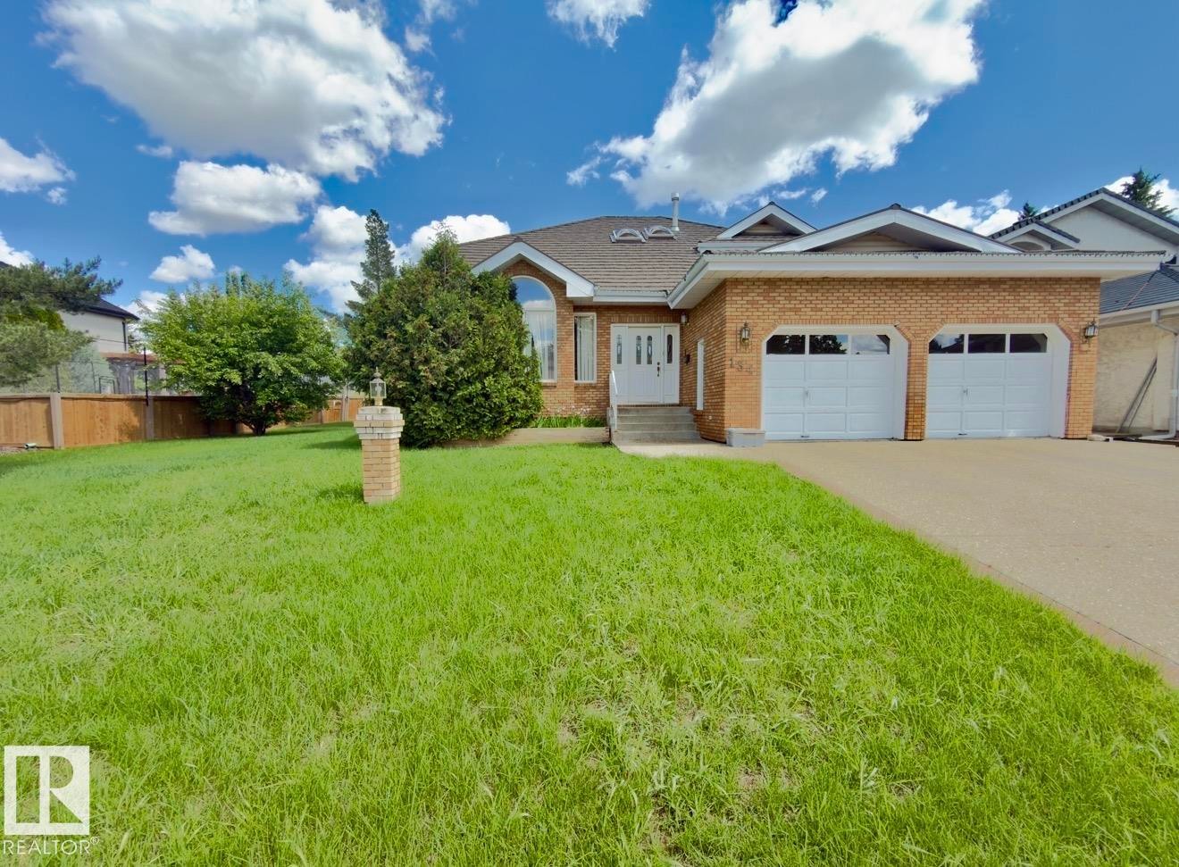 Brick-front residence featuring a two-car garage, concrete driveway, and a manicured front lawn - 134 Wolf Ridge Place, Edmonton, AB