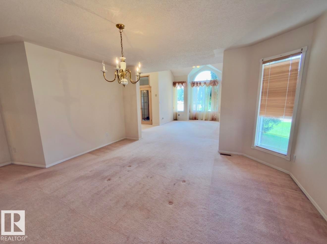 Spacious interior featuring a brass chandelier, multiple windows, arched window, and neutral wall tones - 134 Wolf Ridge Place, Edmonton, AB