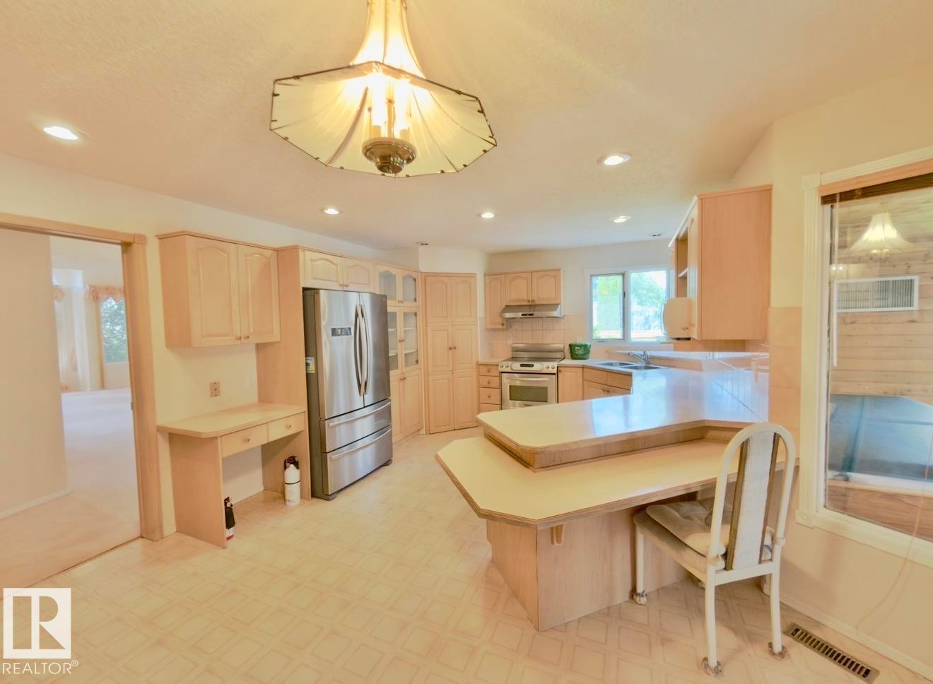 Bright kitchen with light wood-finish cabinetry, stainless steel appliances, recessed lighting, and a built-in desk area - 134 Wolf Ridge Place, Edmonton, AB