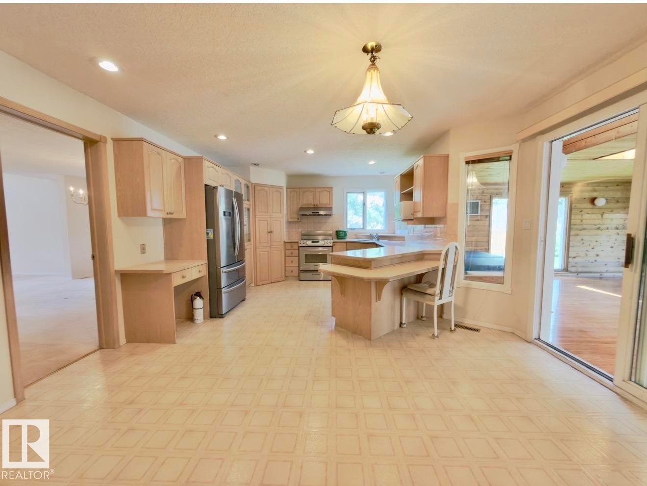 Spacious kitchen featuring light wood cabinetry, stainless steel appliances, a built-in desk area, a breakfast bar with counter seating, and a large sliding glass door - 134 Wolf Ridge Place, Edmonton, AB