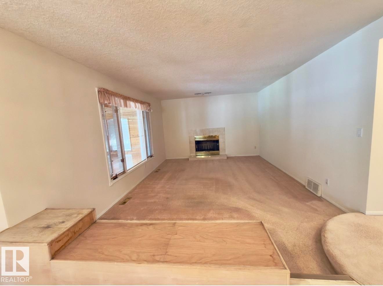 Spacious interior featuring a bay window, an ornate fireplace with a brass firebox, and a built-in multi-level platform - 134 Wolf Ridge Place, Edmonton, AB