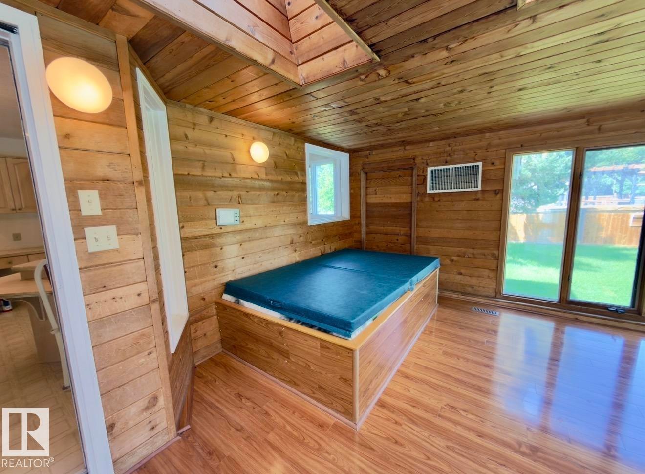Interior space featuring wood-finish walls and ceiling, a built-in spa, wood-finish flooring, and large windows with outdoor visibility - 134 Wolf Ridge Place, Edmonton, AB