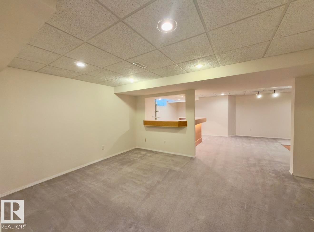 Spacious finished basement featuring recessed lighting, a drop ceiling, light gray carpeting, a built-in bar with wood-finish countertop, and white painted walls - 134 Wolf Ridge Place, Edmonton, AB