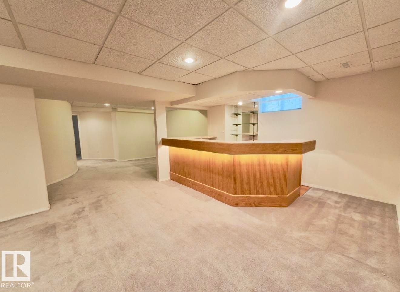 Finished lower level featuring a built-in bar with under-cabinet lighting, glass shelving, recessed lighting, and light-toned carpeting - 134 Wolf Ridge Place, Edmonton, AB