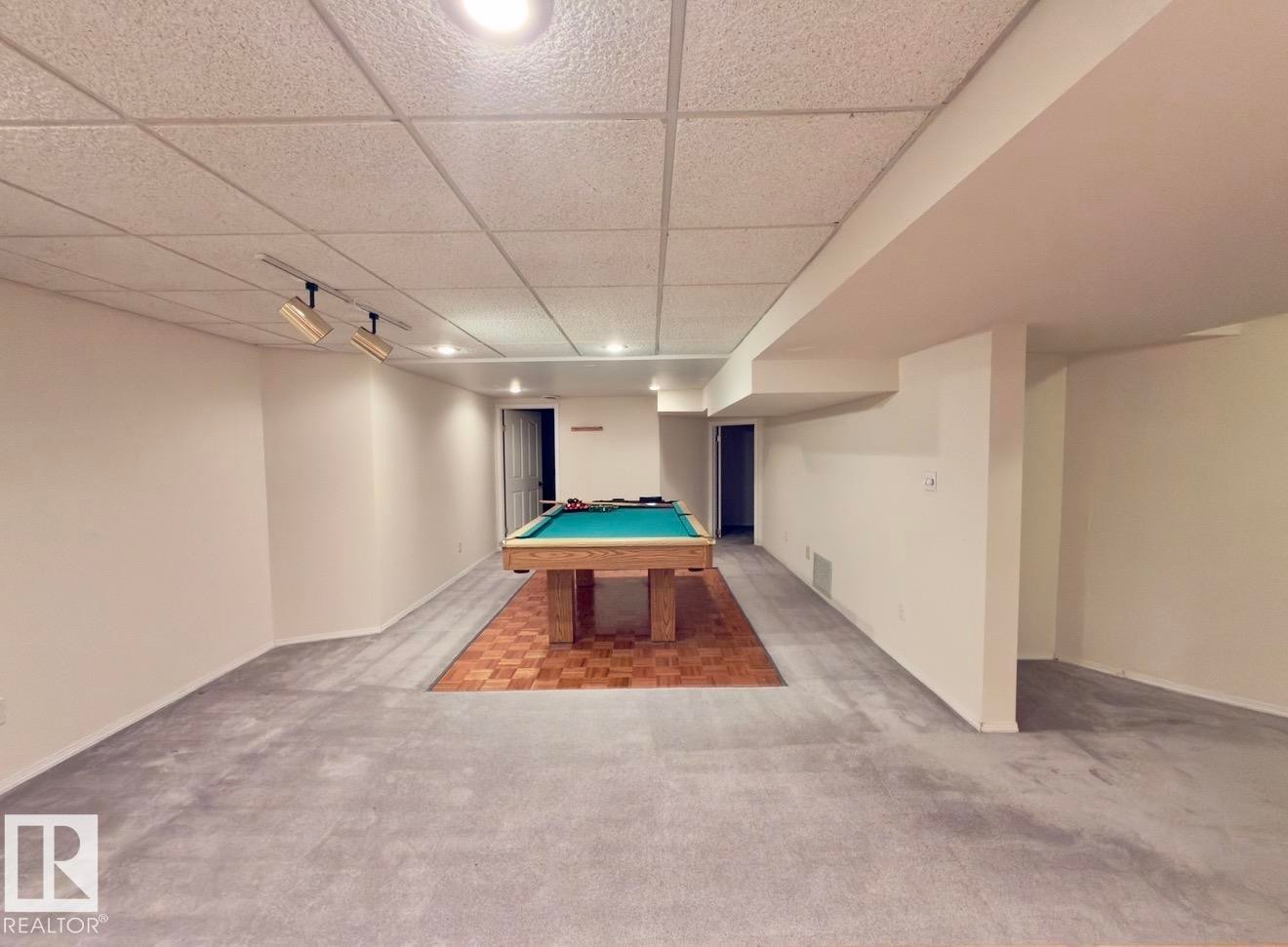 Expansive recreation room featuring a drop ceiling with recessed lighting and track lighting, grey carpeting, and a wood-finish flooring section - 134 Wolf Ridge Place, Edmonton, AB
