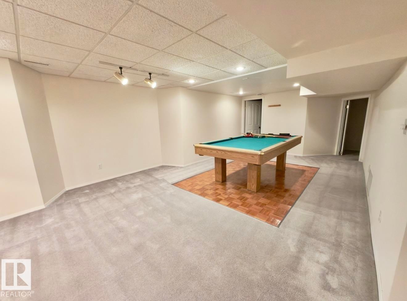 Spacious recreational room featuring light gray carpeting, a section of square wood-finish flooring, and recessed lighting - 134 Wolf Ridge Place, Edmonton, AB