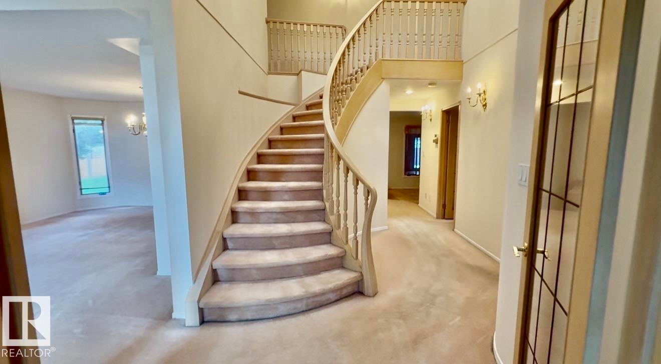 Grand entryway featuring a curved staircase with wood banister and balusters, carpeted stairs, and upper-level landing - 134 Wolf Ridge Place, Edmonton, AB