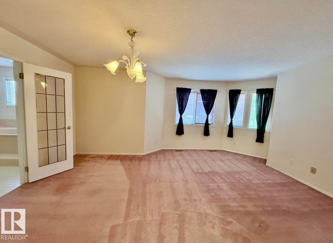 Spacious interior room featuring a bay window, a ceiling-mounted light fixture, and a glass-paneled door - 134 Wolf Ridge Place, Edmonton, AB